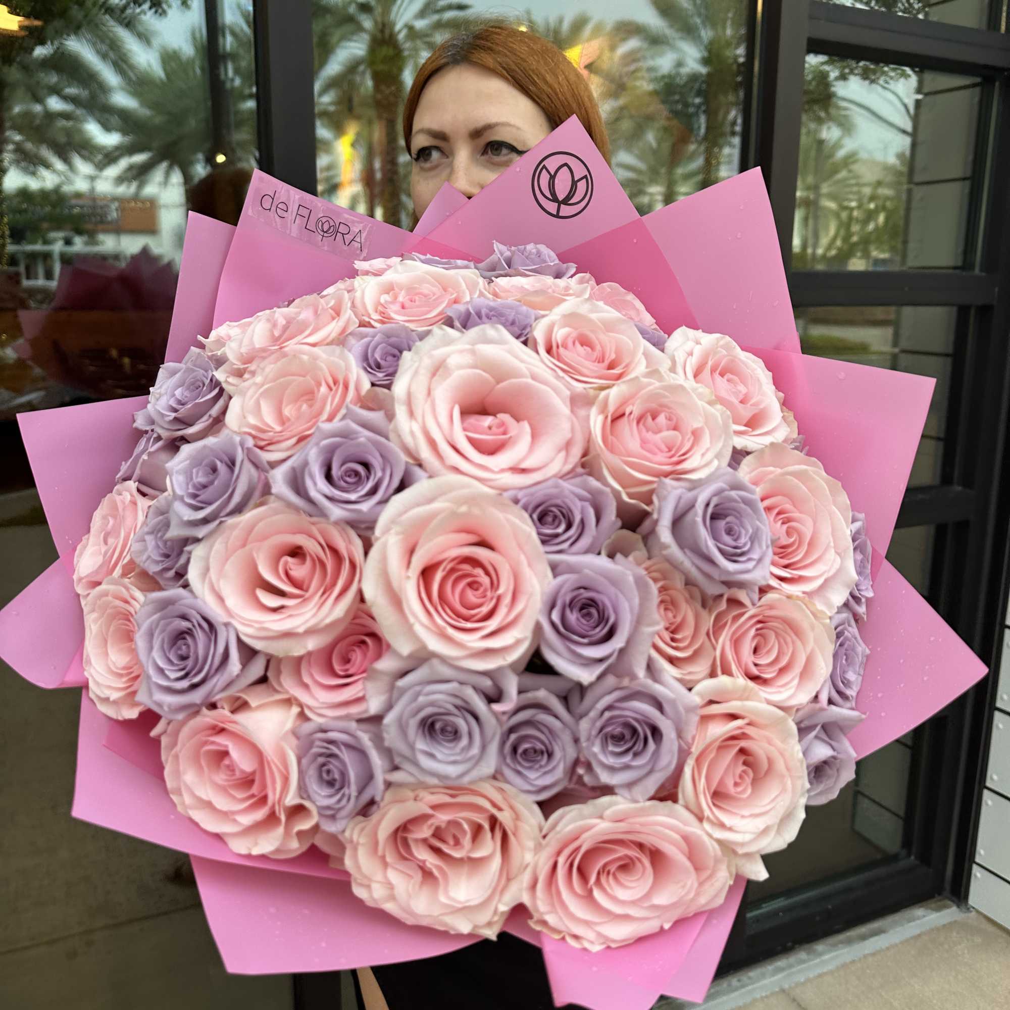 Large hand-tied bouquet of pink and lavender roses wrapped in bright pink paper.