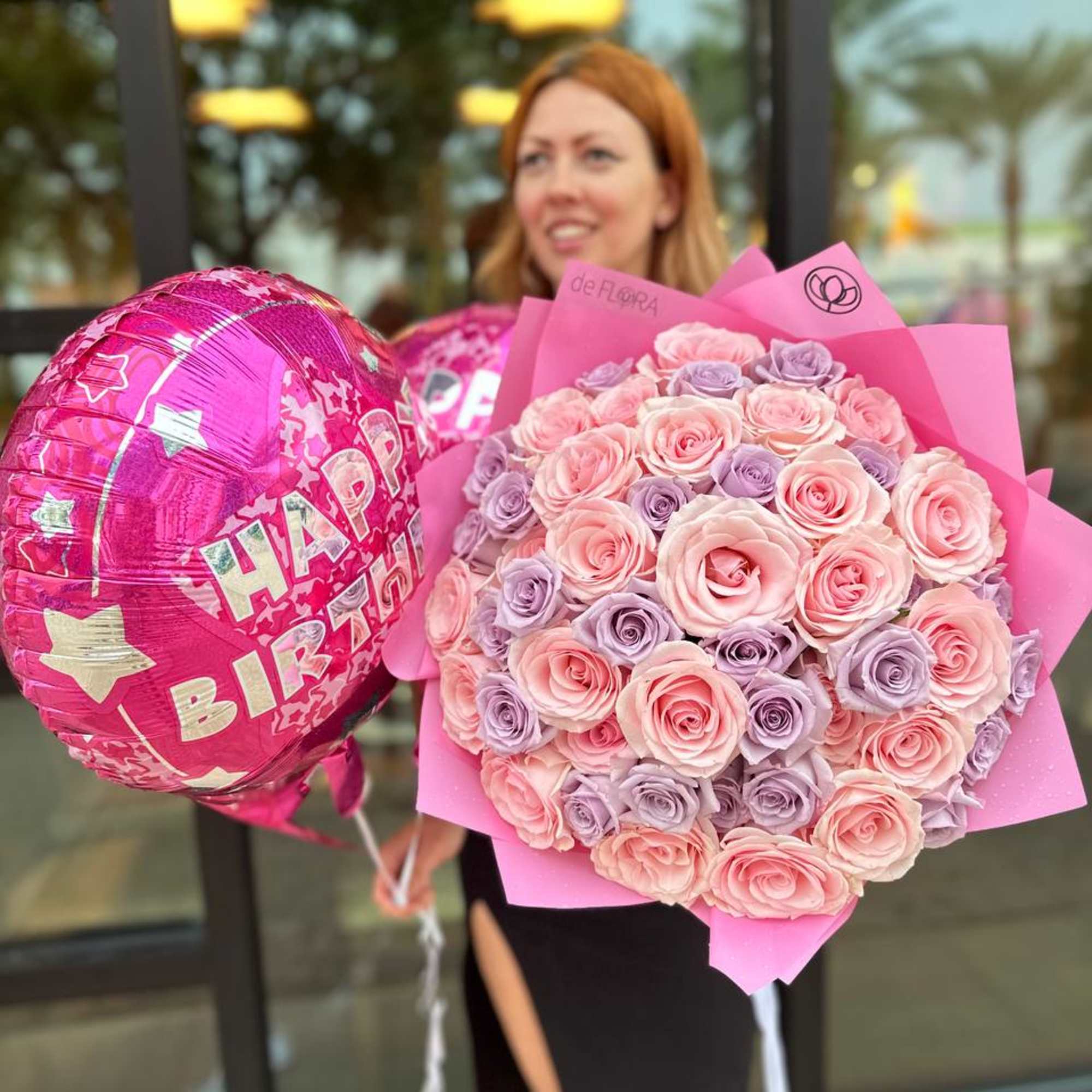 Large bouquet of pink and lavender roses wrapped in pink paper with matching Happy Birthday balloons.