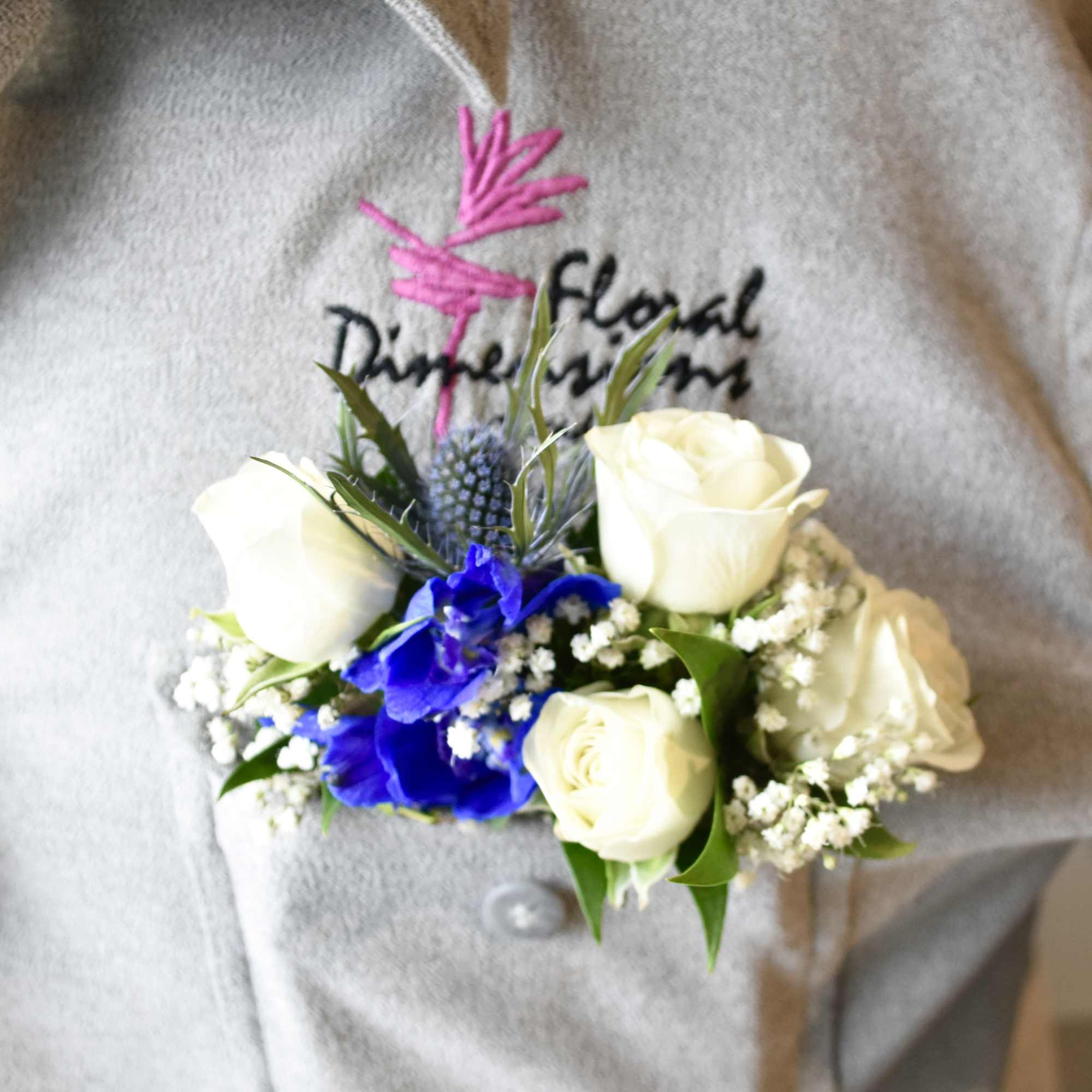 Boutonniere with white roses and blue flowers on a gray jacket