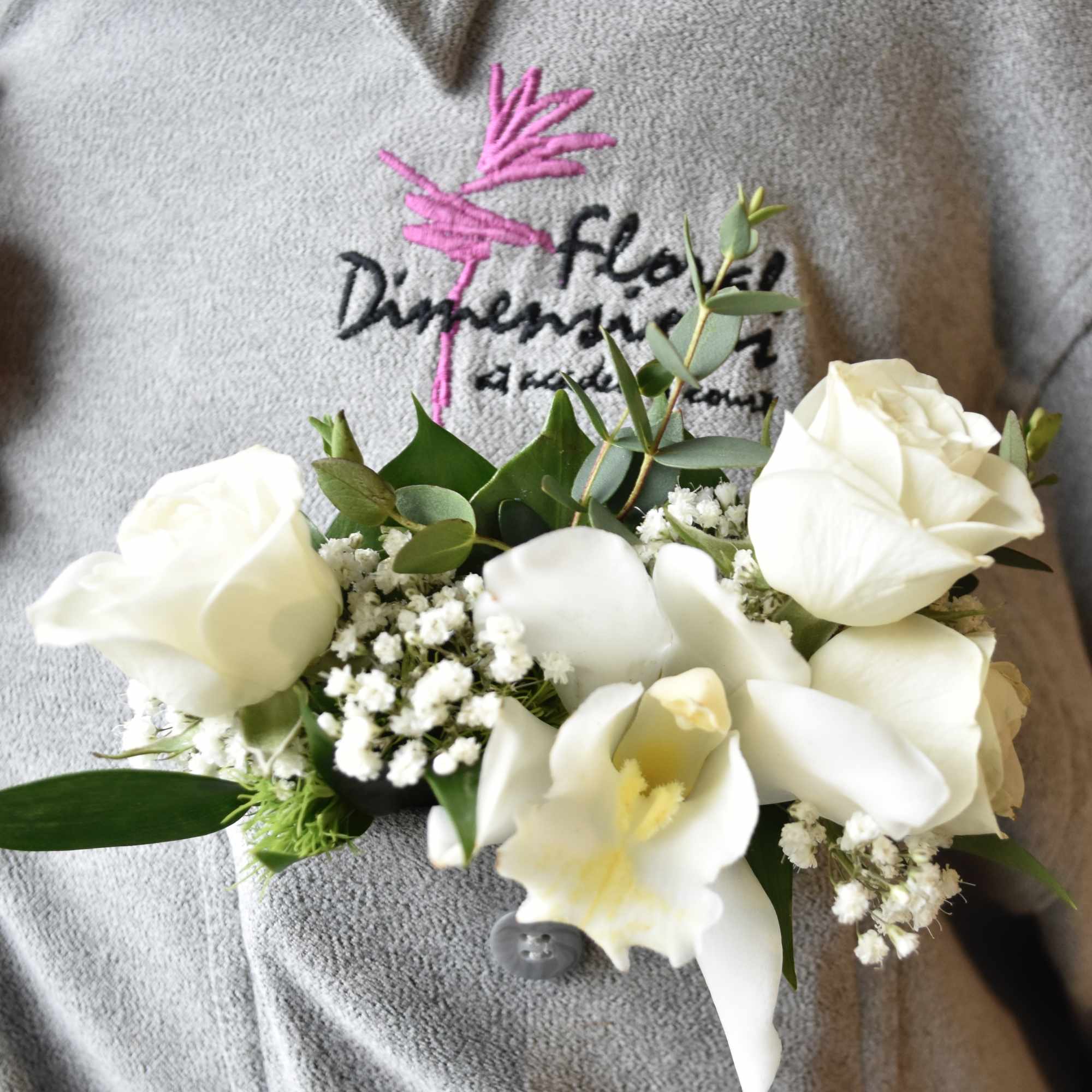 White floral corsage with roses and calla lilies on a gray sweater