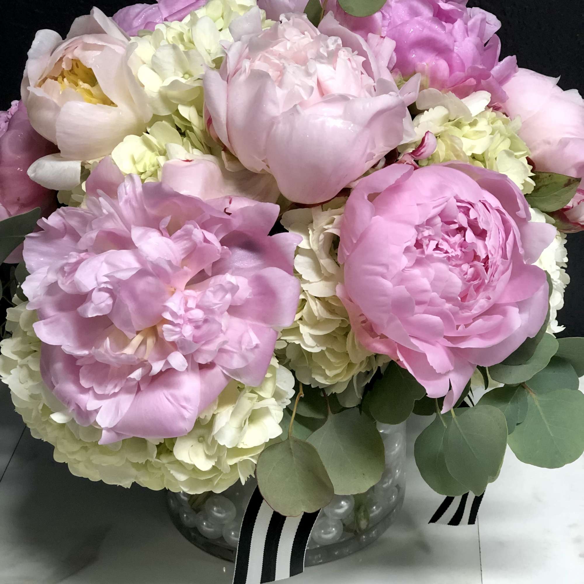Pink peonies and pale hydrangeas in a glass vase with eucalyptus.