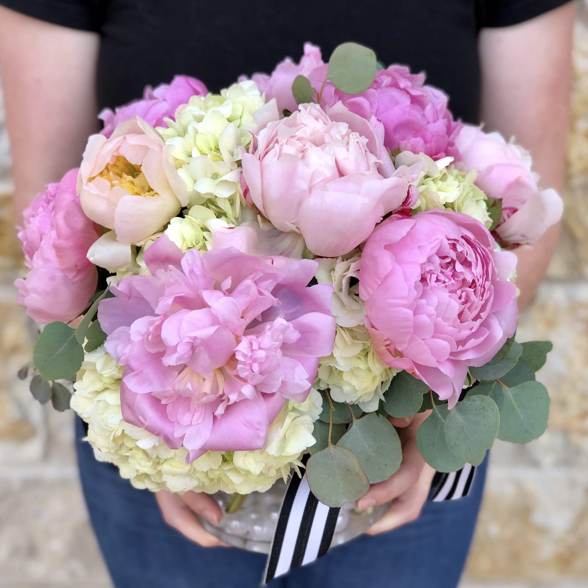 Pink peonies and pale hydrangeas in a clear vase with eucalyptus