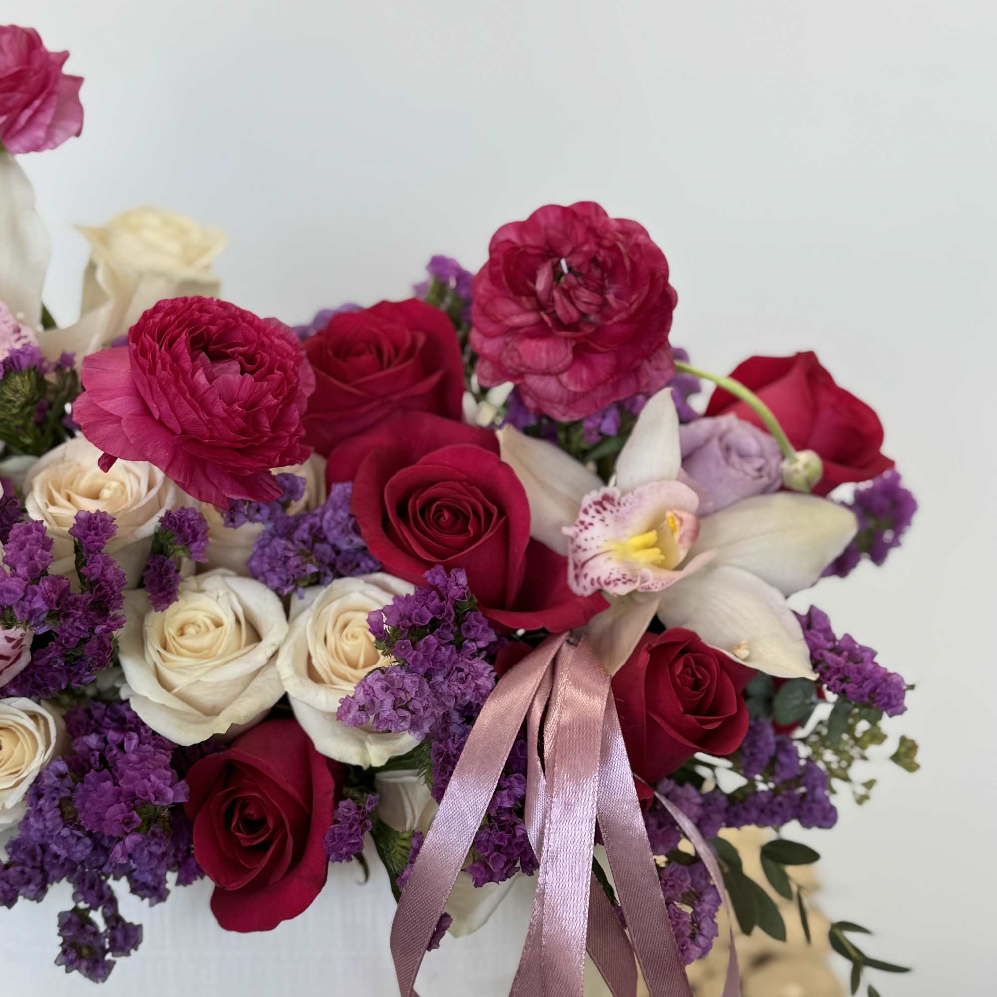 Bouquet of red and cream roses with purple flowers and a pink ribbon
