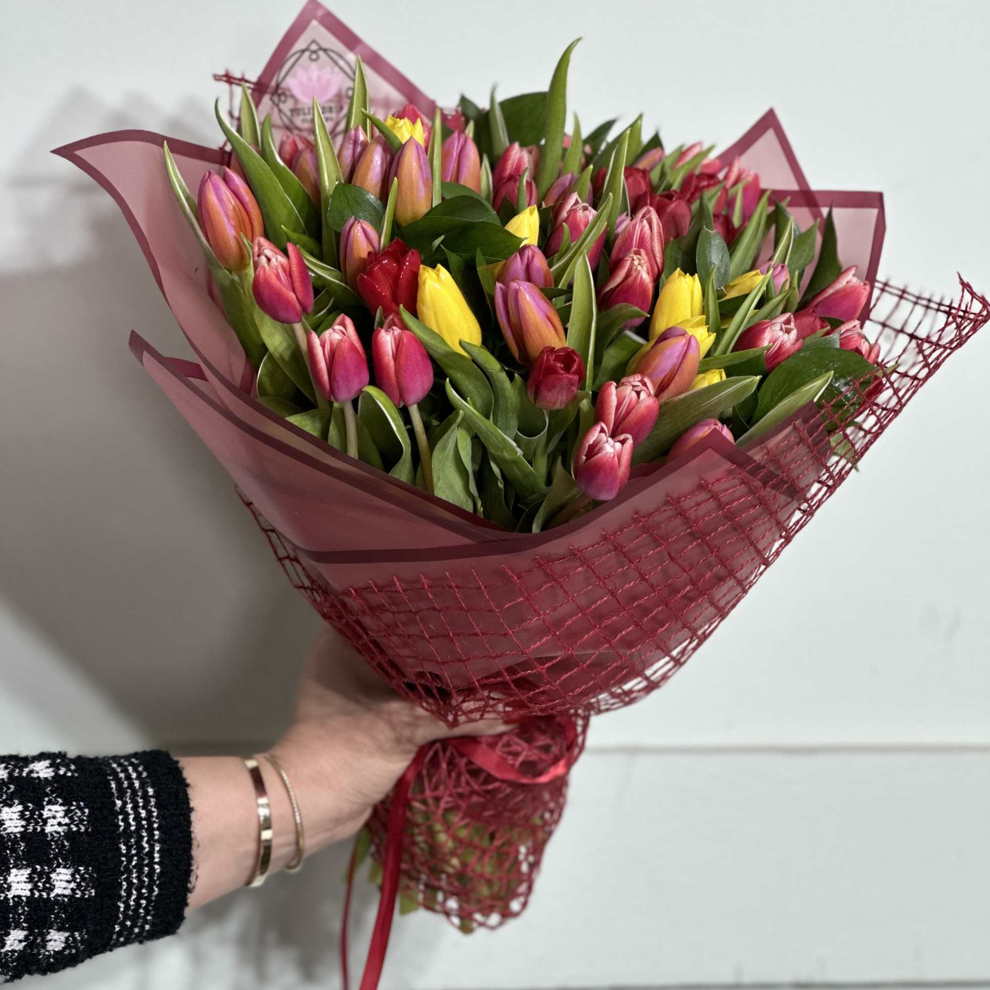 Handheld bouquet of pink, yellow, and orange tulips wrapped in magenta paper
