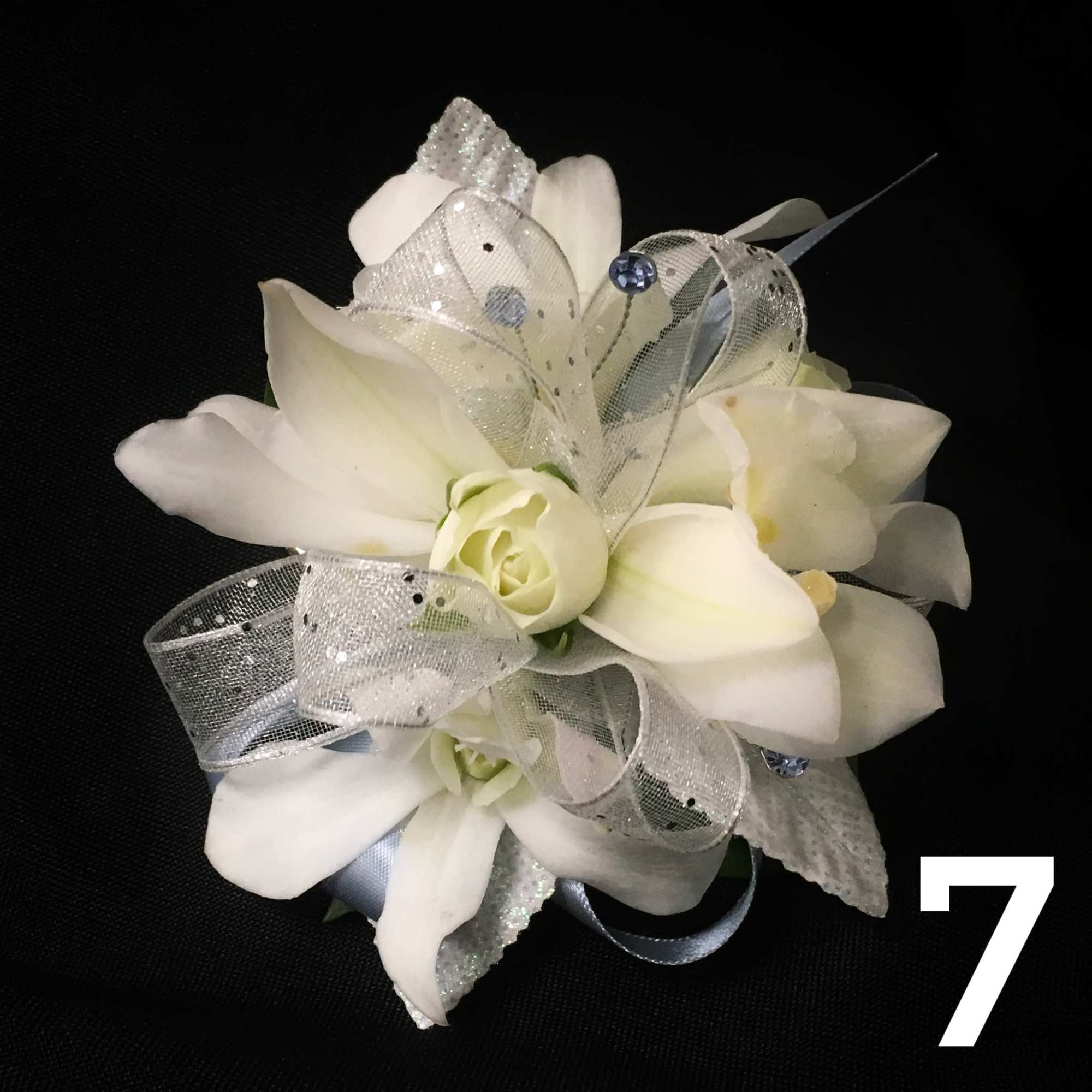 White floral corsage with silver ribbon on a black background