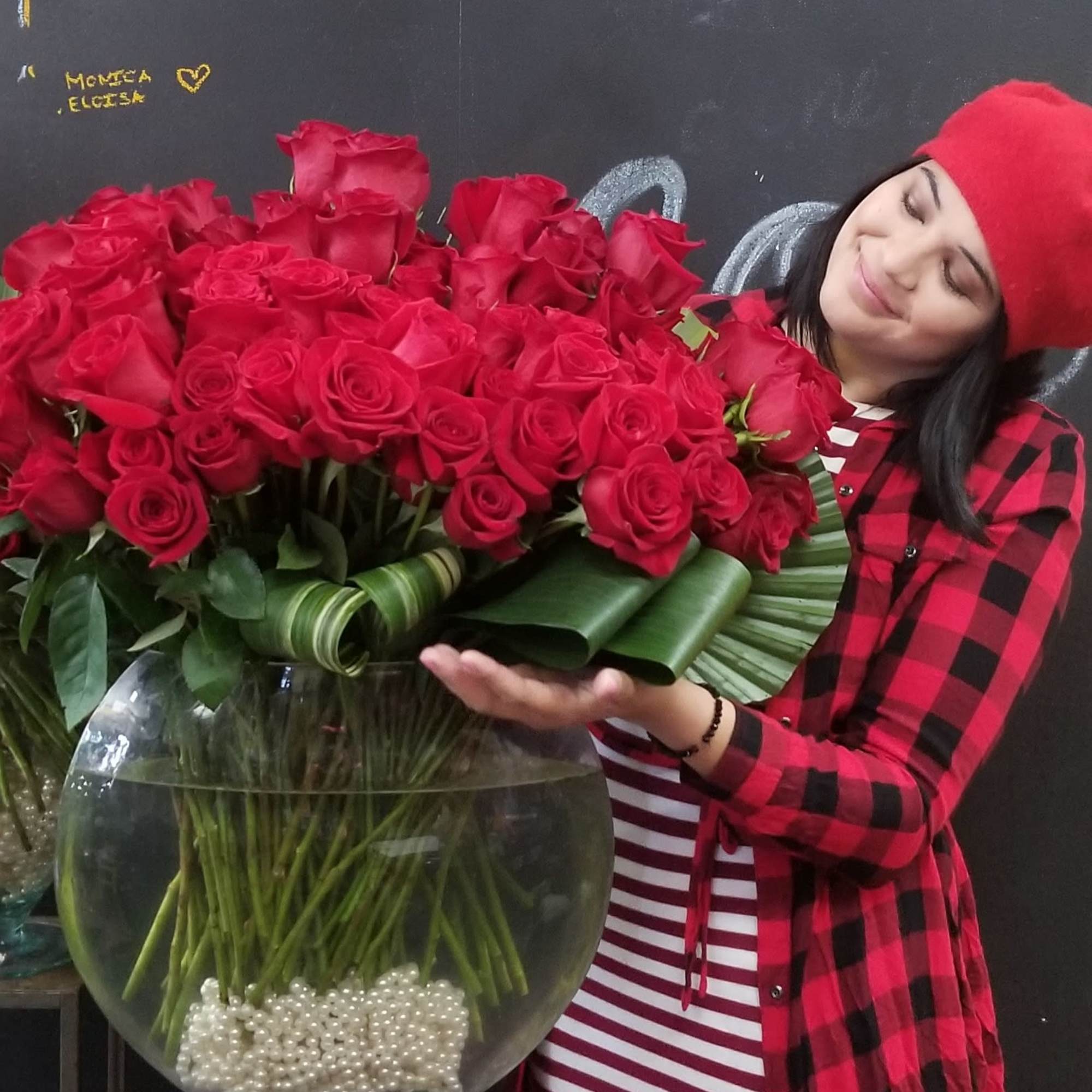 Large bouquet of red roses in a glass vase with a woman in a red hat beside it