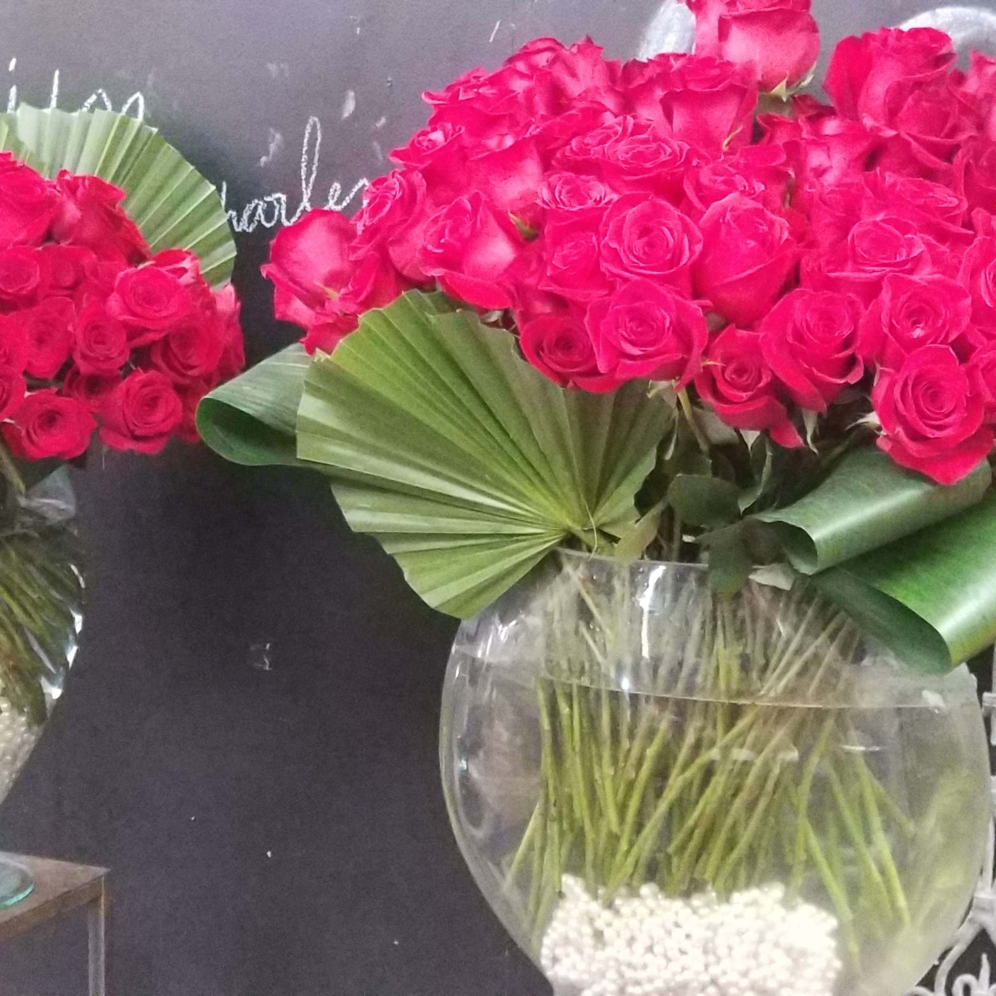 Two vases of bright pink roses with large green leaves