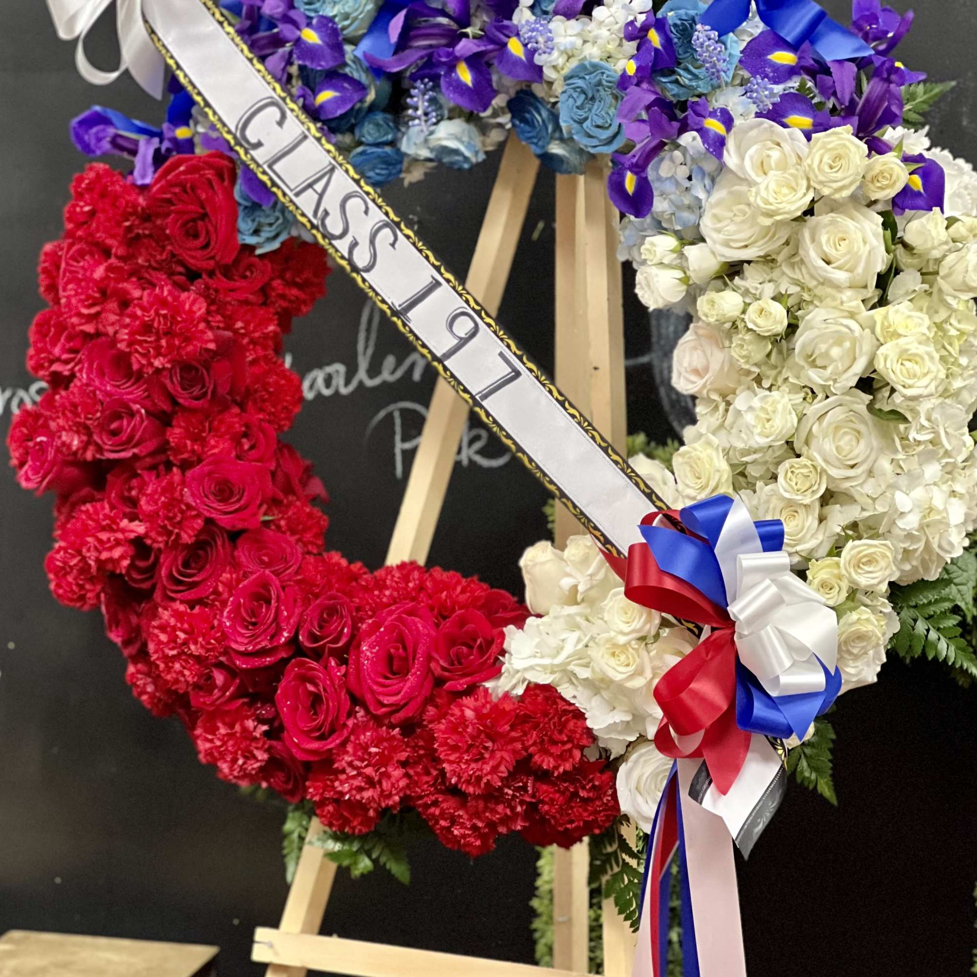 Heart-shaped floral wreath with red, white, and blue flowers on an easel