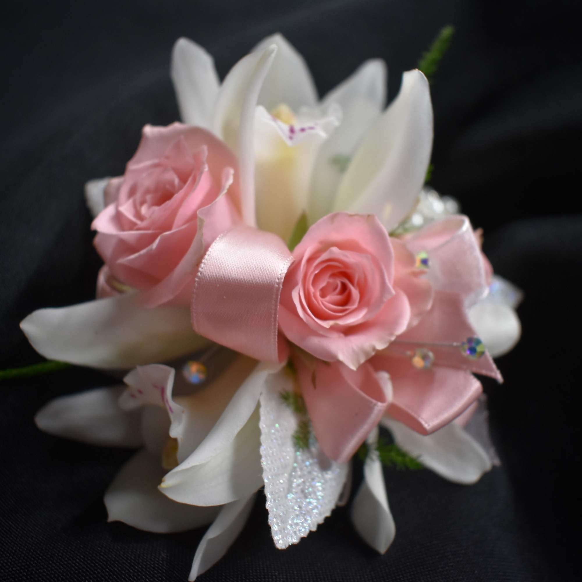 Pink roses and white lilies with a pink ribbon on a dark background