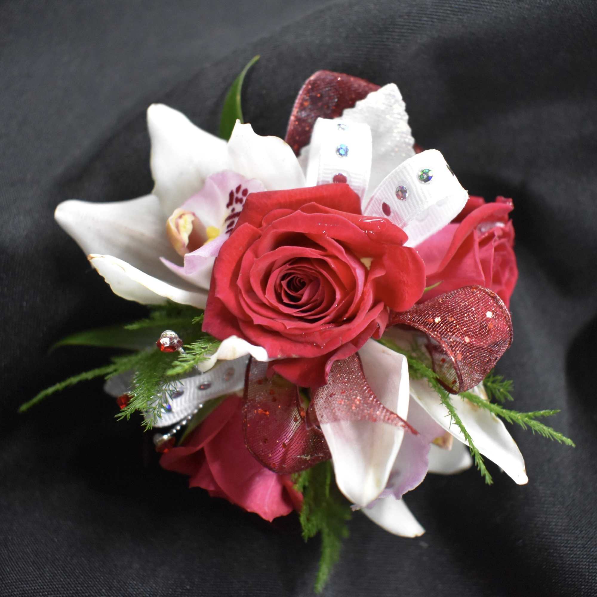 Red rose corsage with white lilies and ribbon on a dark background