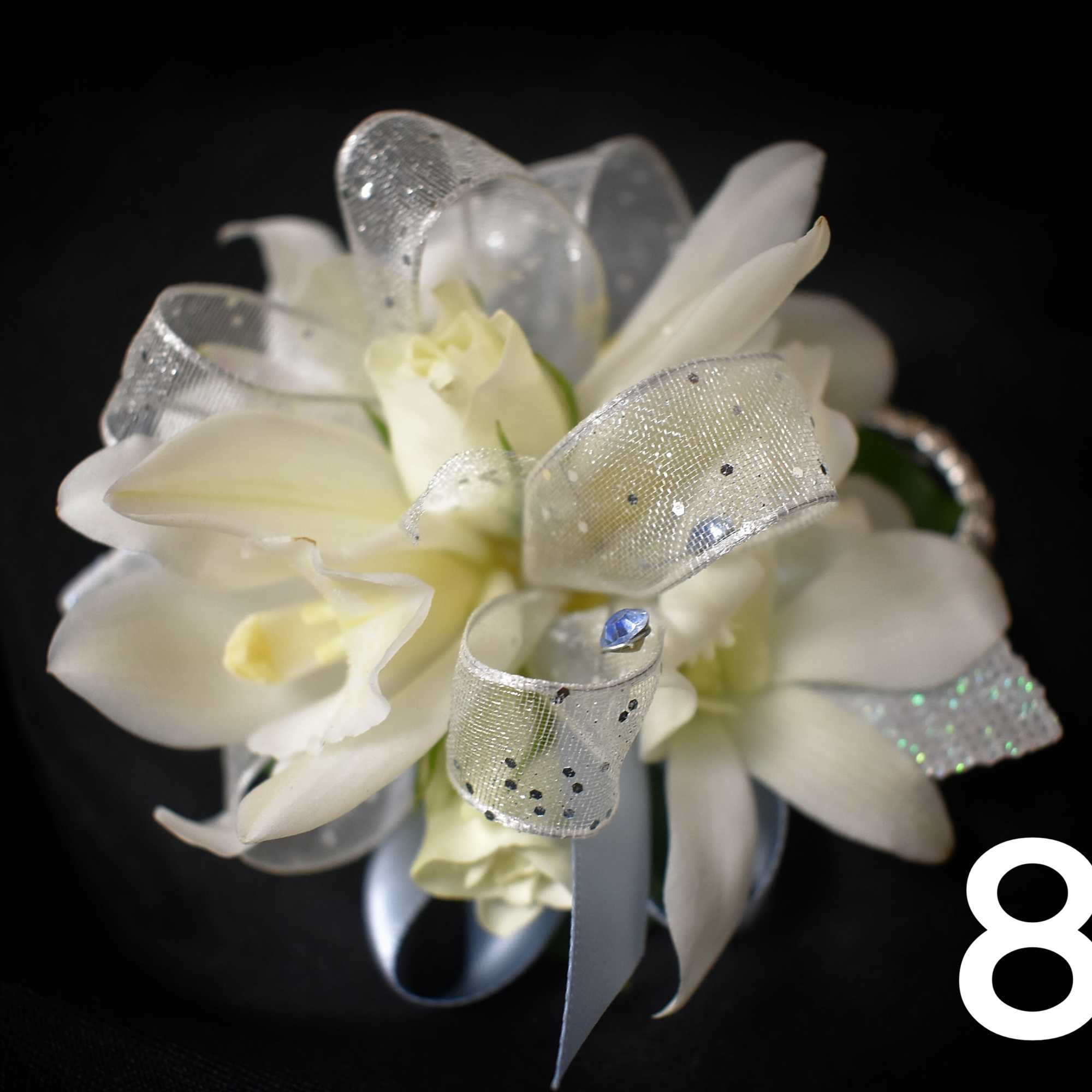 White orchid corsage with silver ribbon on a black background