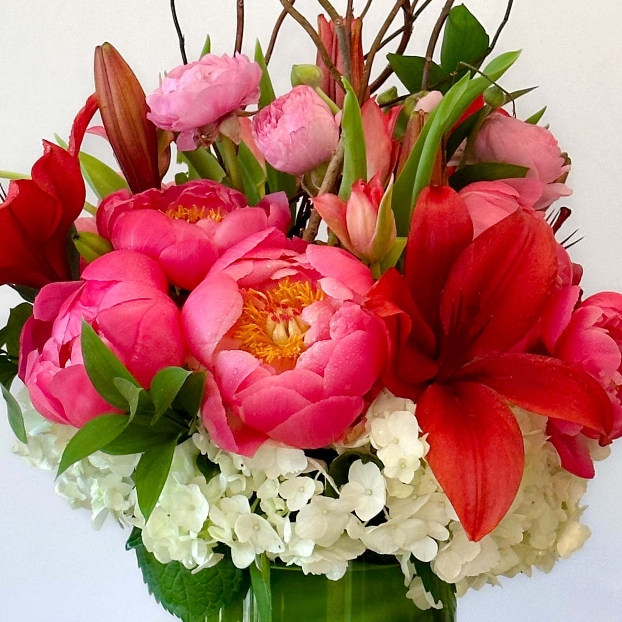 Pink peonies and red lilies in a green vase with white hydrangeas
