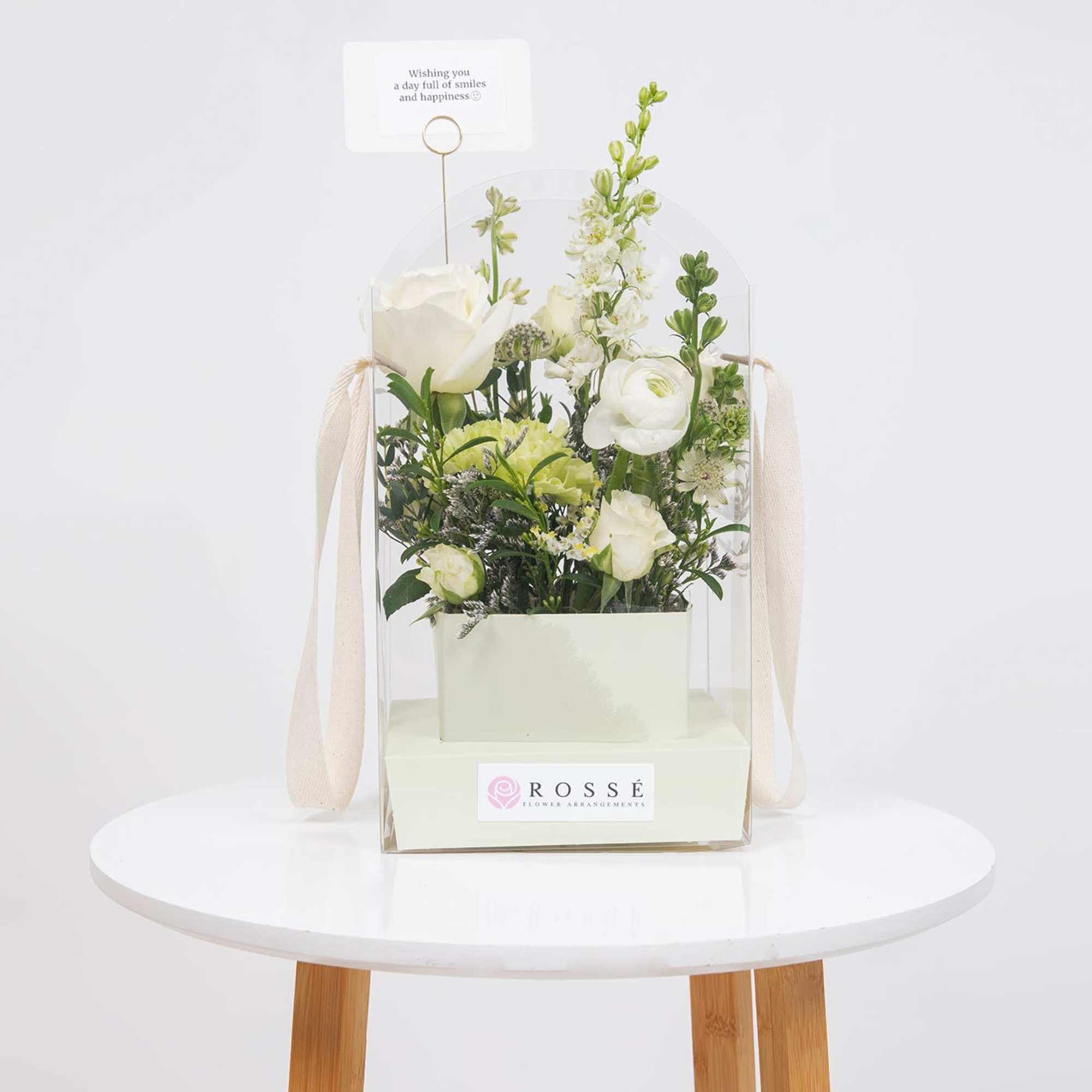 White floral arrangement in a clear gift box with a small card topper