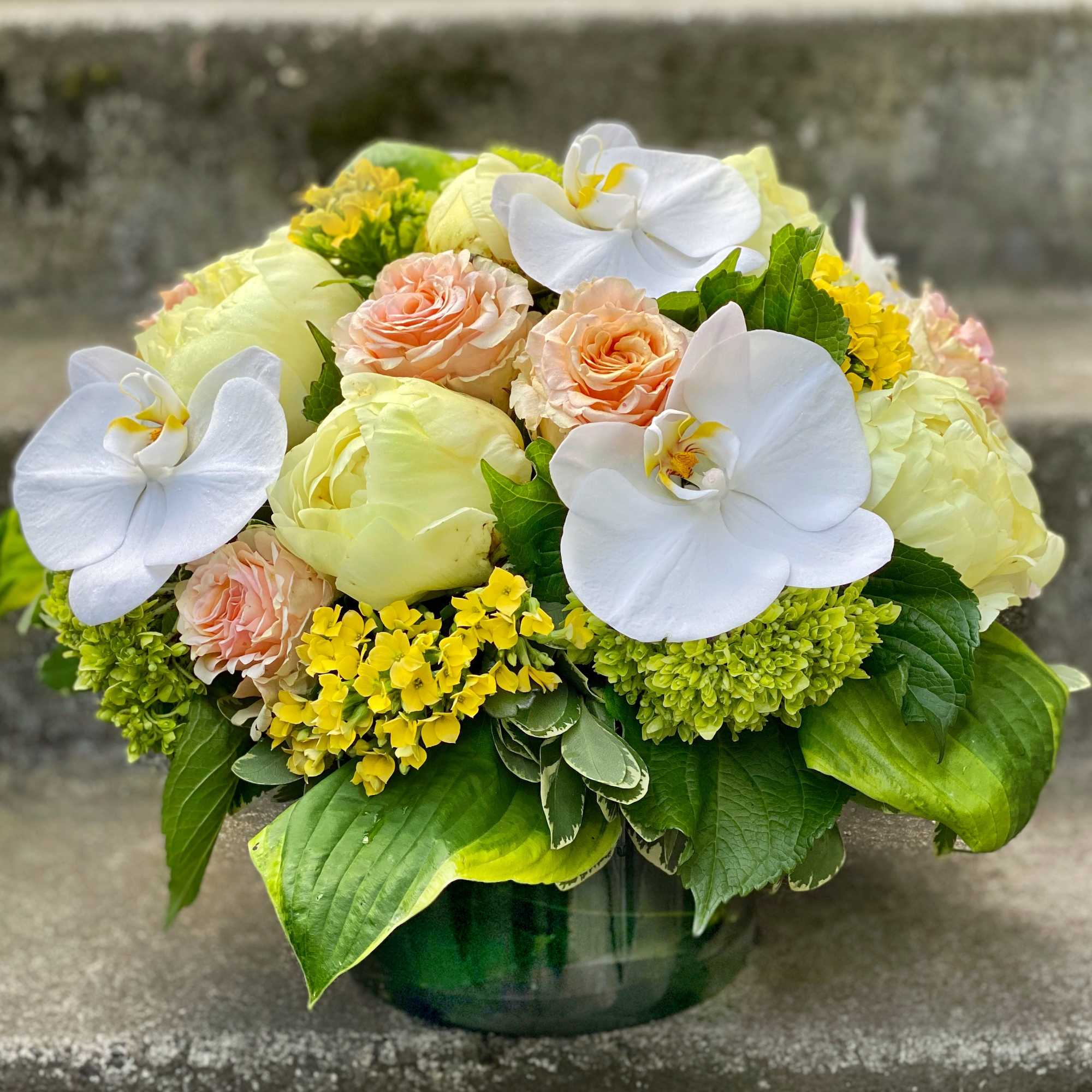 Bouquet of white orchids, pale roses, and yellow blooms in a green vase