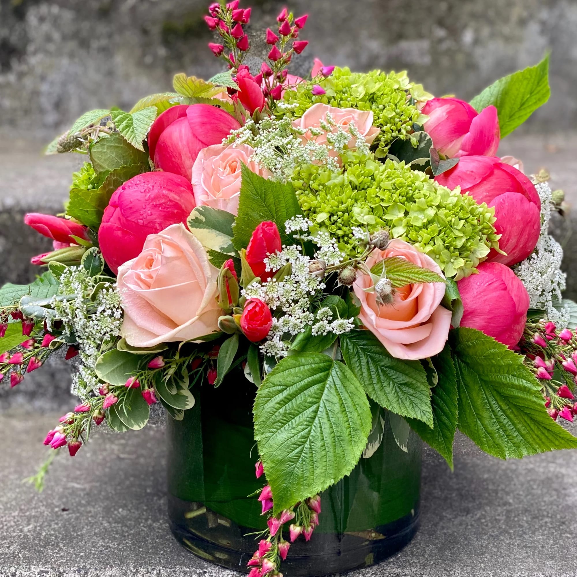 Pink roses and peonies in a dark glass vase with green hydrangeas