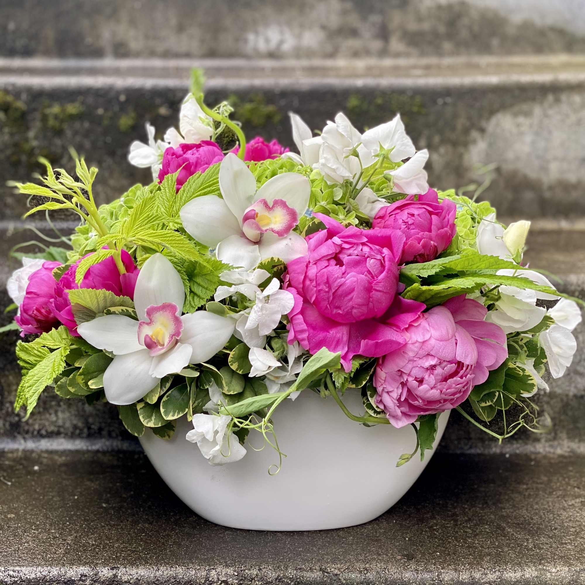 Pink peonies and white orchids in a white bowl vase