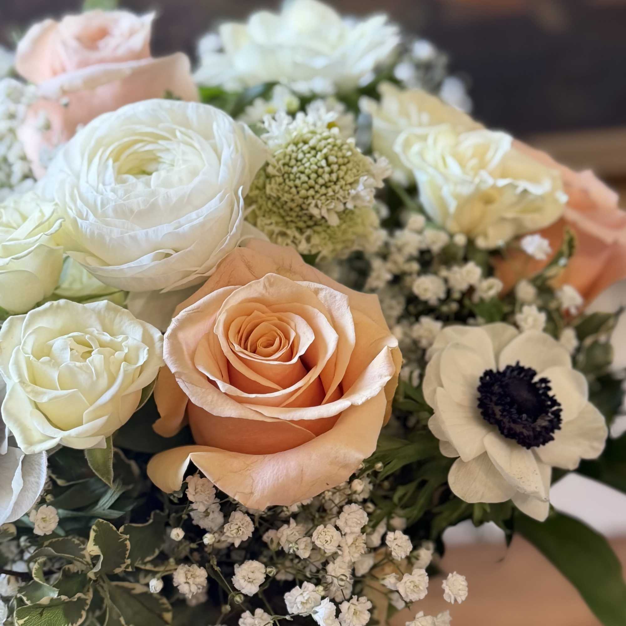 Peach and white rose bouquet with ranunculus, anemone, and baby's breath in a clear glass vase