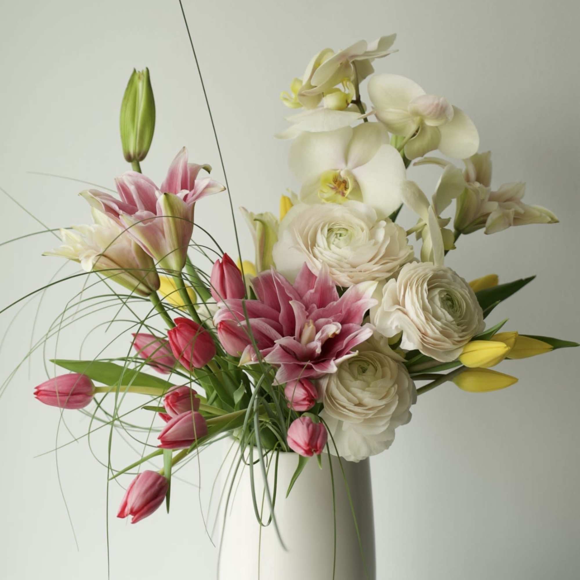 A modern garden-style arrangement featuring delicate pink lilies, premium white ranunculus, soft