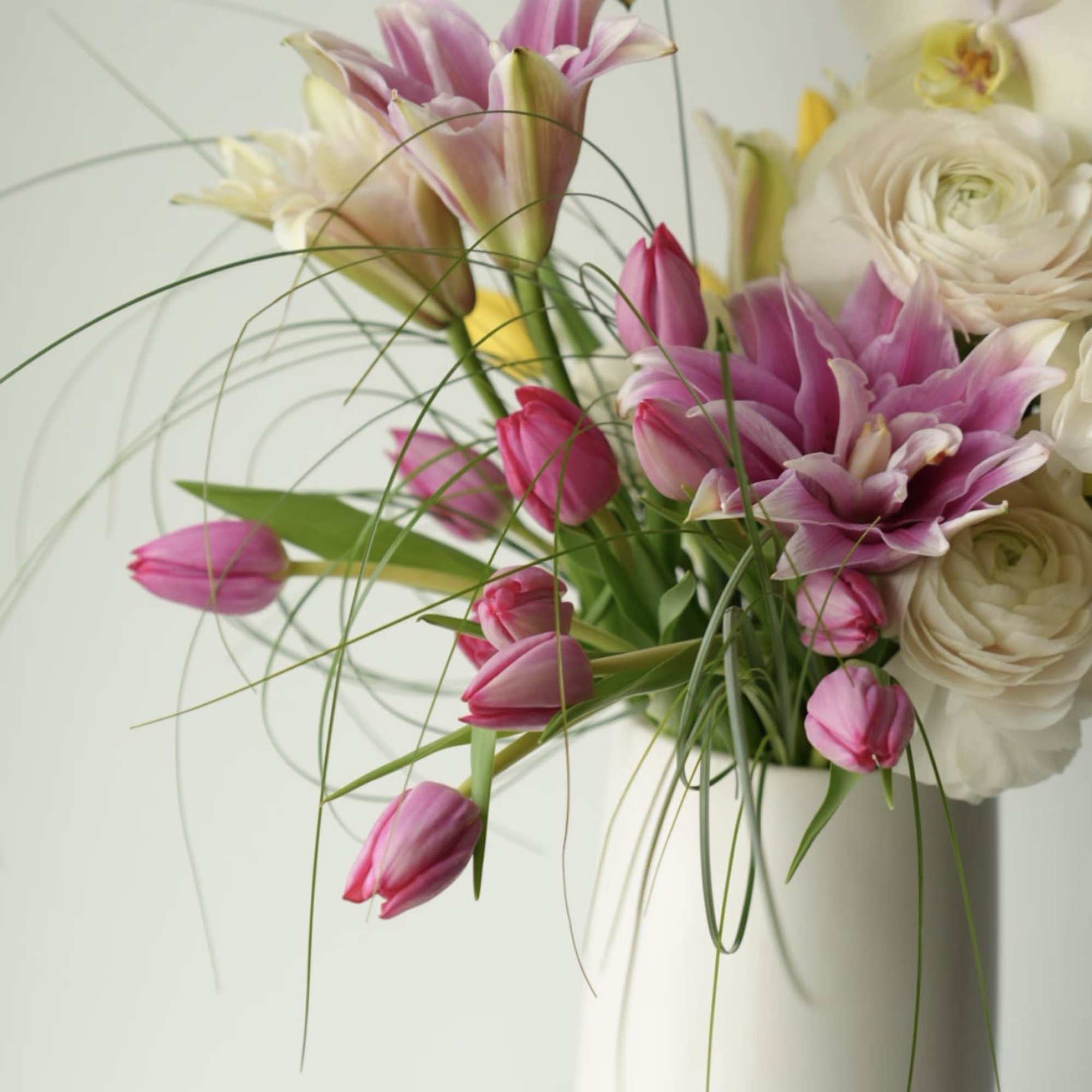 A modern garden-style arrangement featuring delicate pink lilies, premium white ranunculus, soft