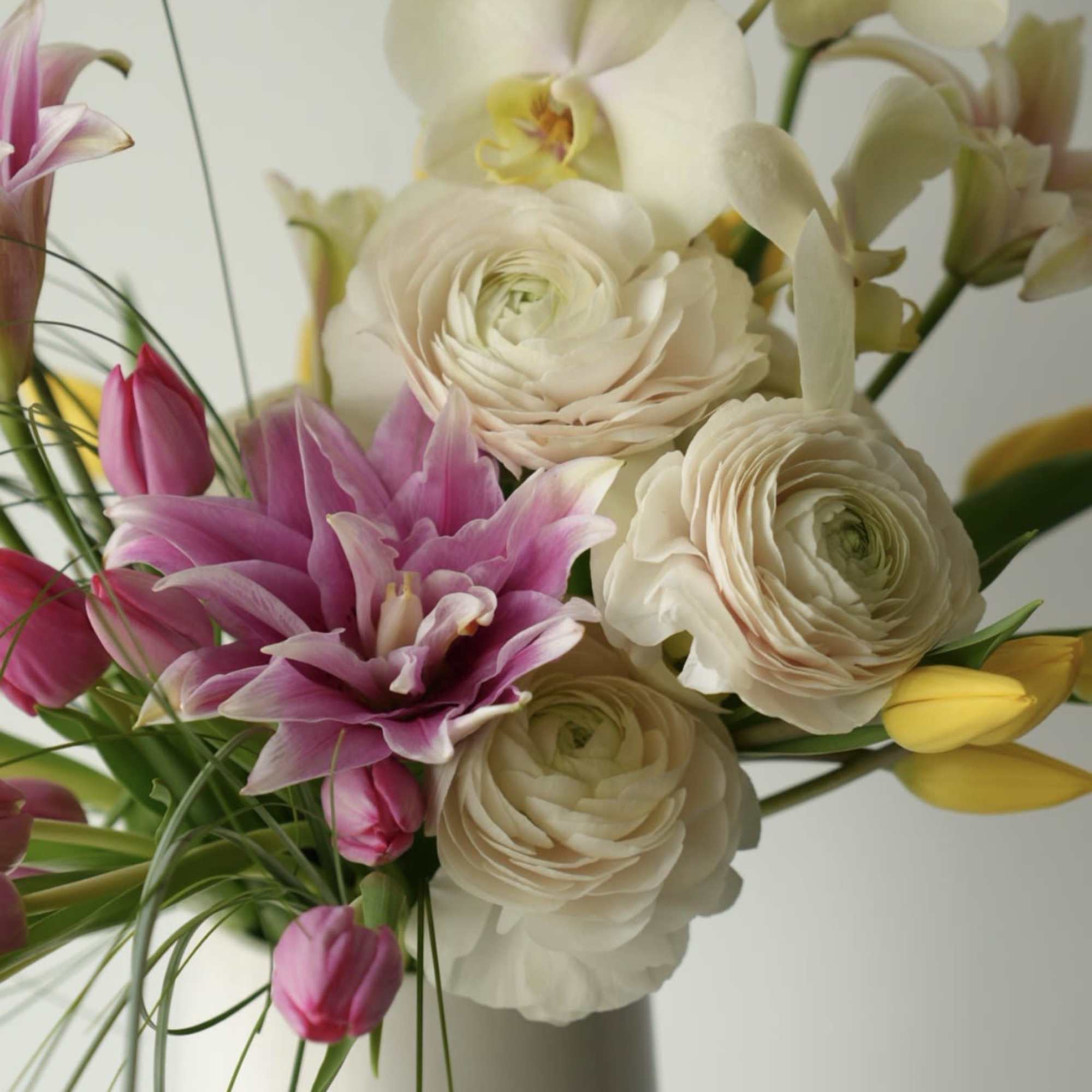A modern garden-style arrangement featuring delicate pink lilies, premium white ranunculus, soft