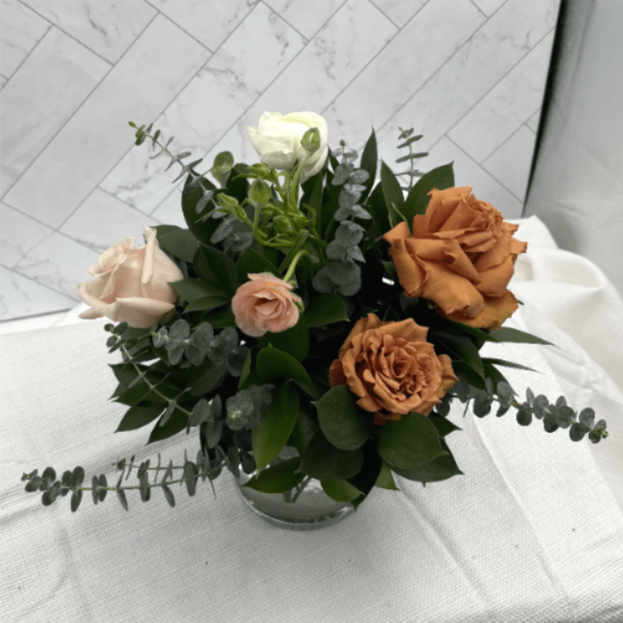 Low arrangement of tan and peach roses with white lisianthus in a clear glass bowl vase.