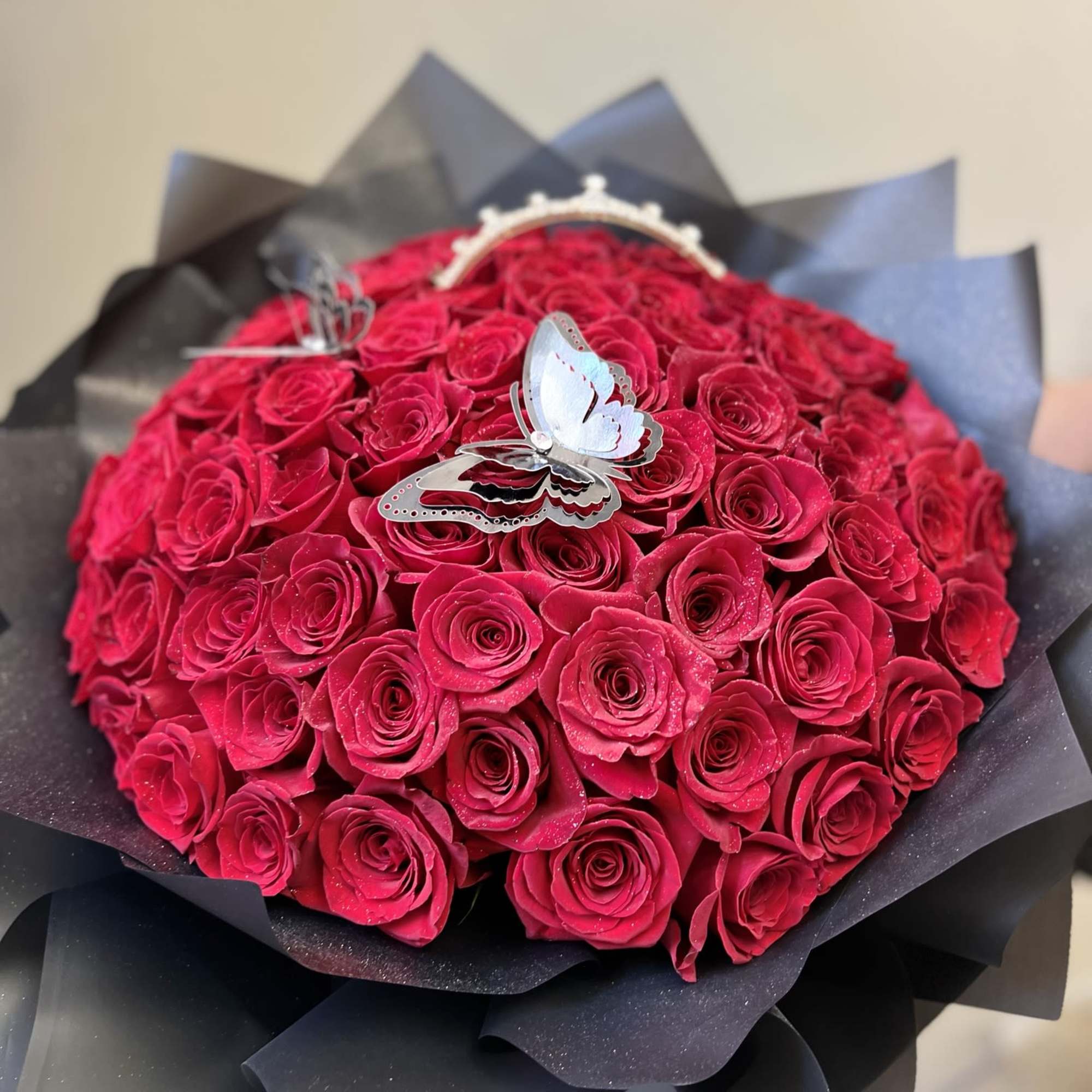 Bouquet of bright pink roses wrapped in black paper with a butterfly topper