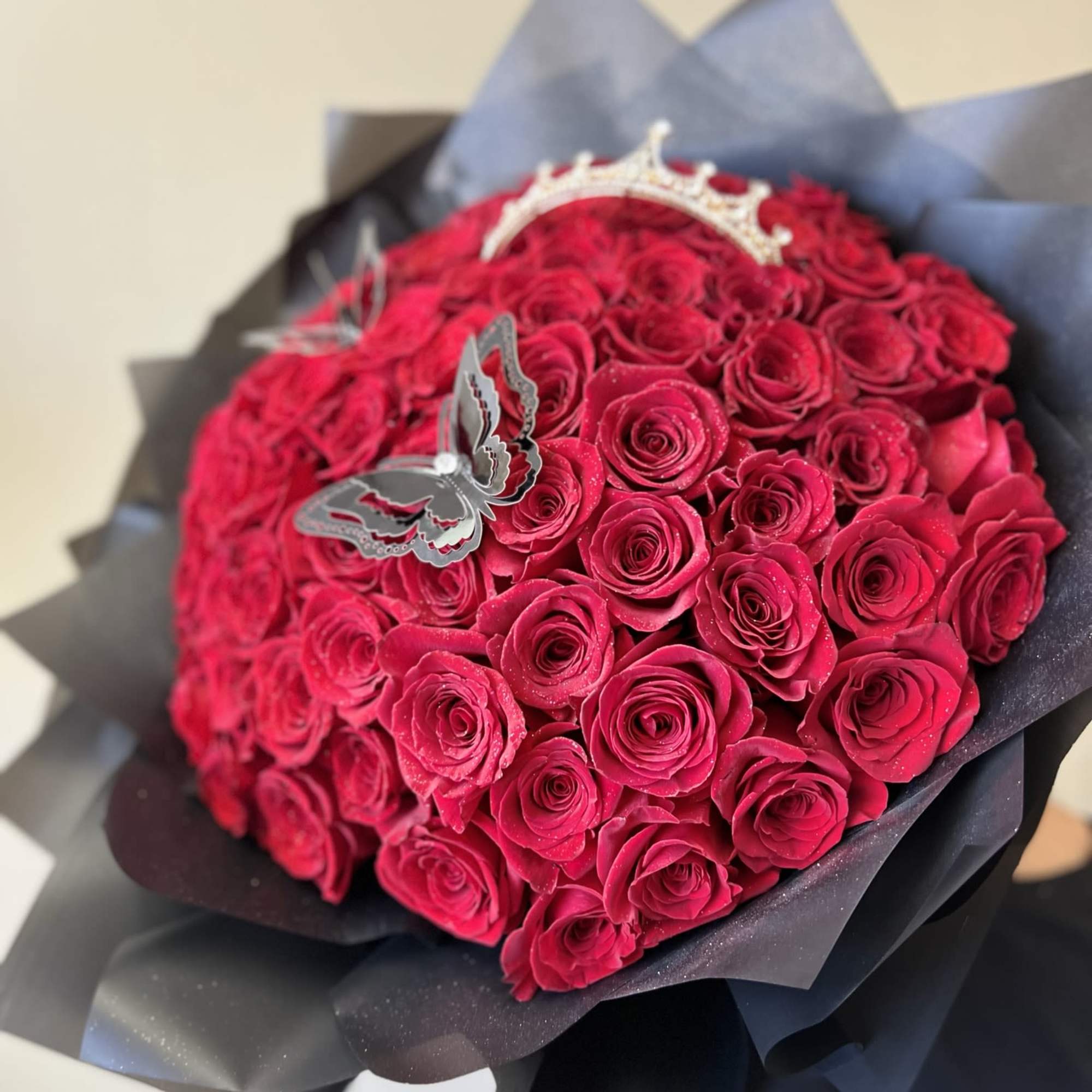 Bouquet of red roses wrapped in dark paper with a butterfly topper