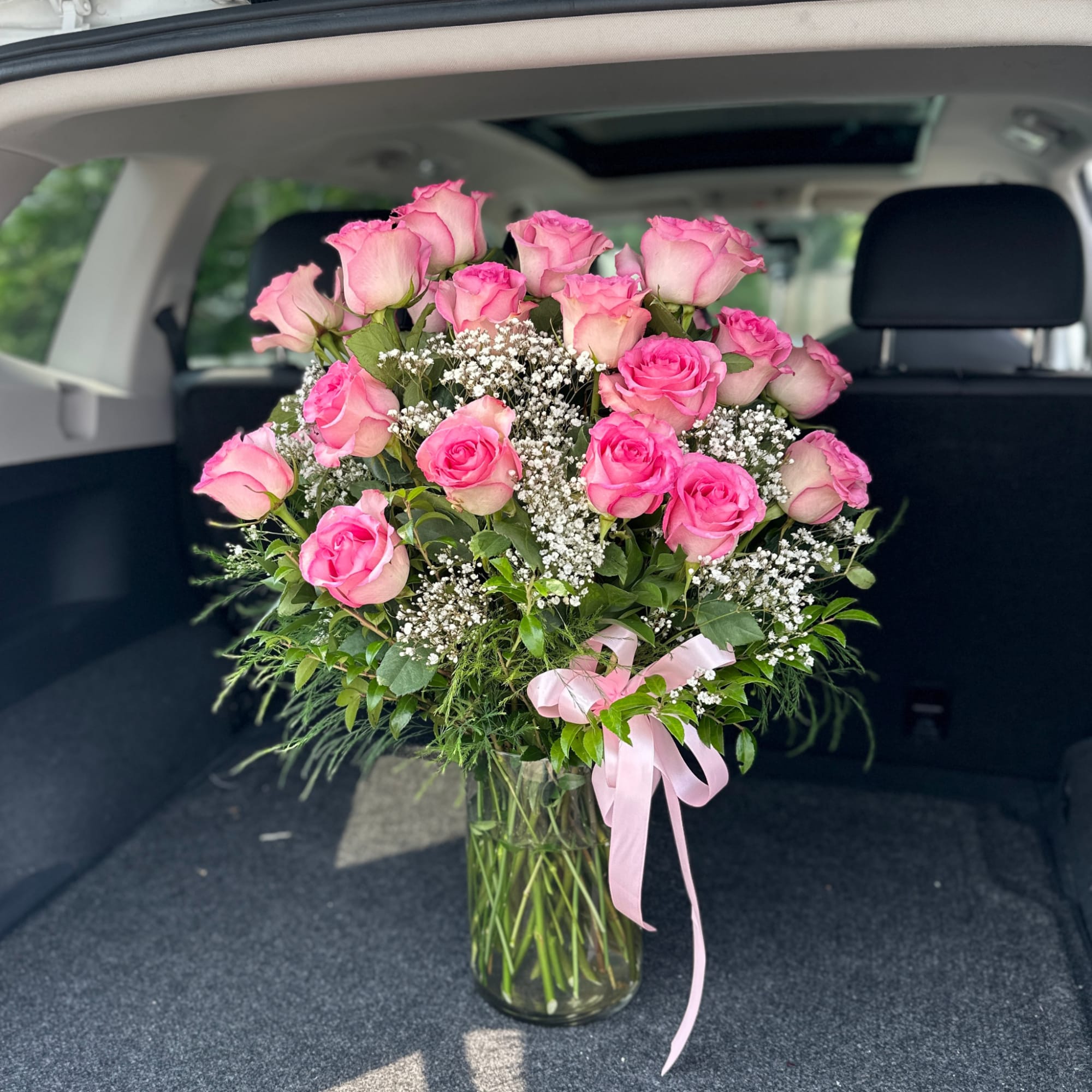 Pink roses arranged in a clear glass vase with baby's breath and a pink ribbon