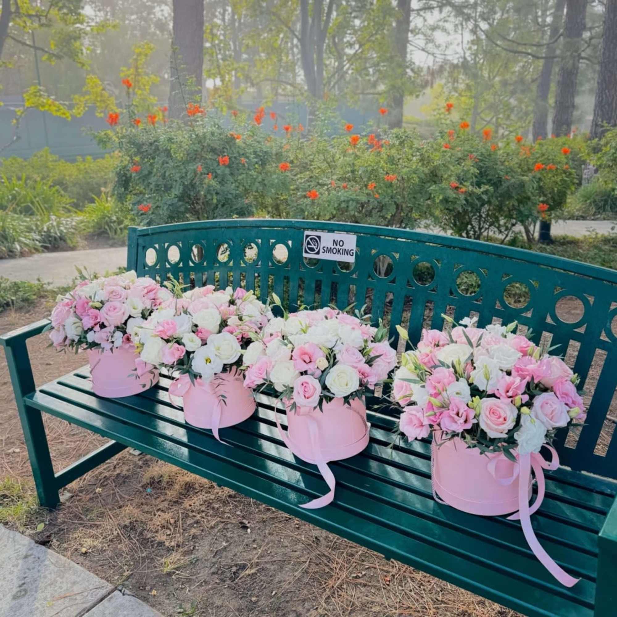 Four pink hatbox bouquets of pink and white roses on a green bench