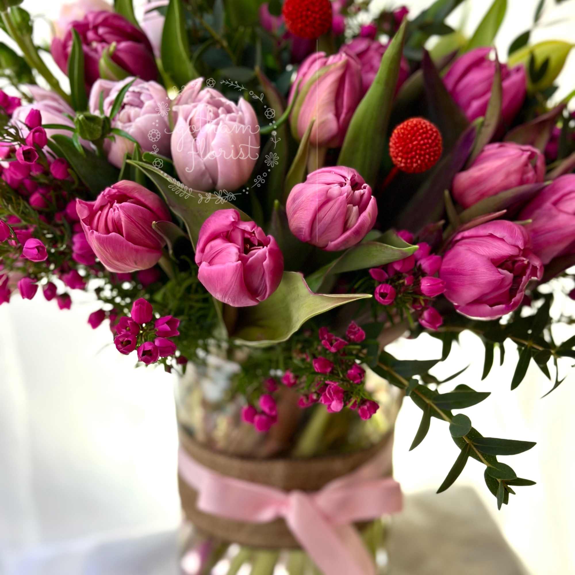 Pink tulips and magenta flowers arranged in a glass vase with a pink ribbon