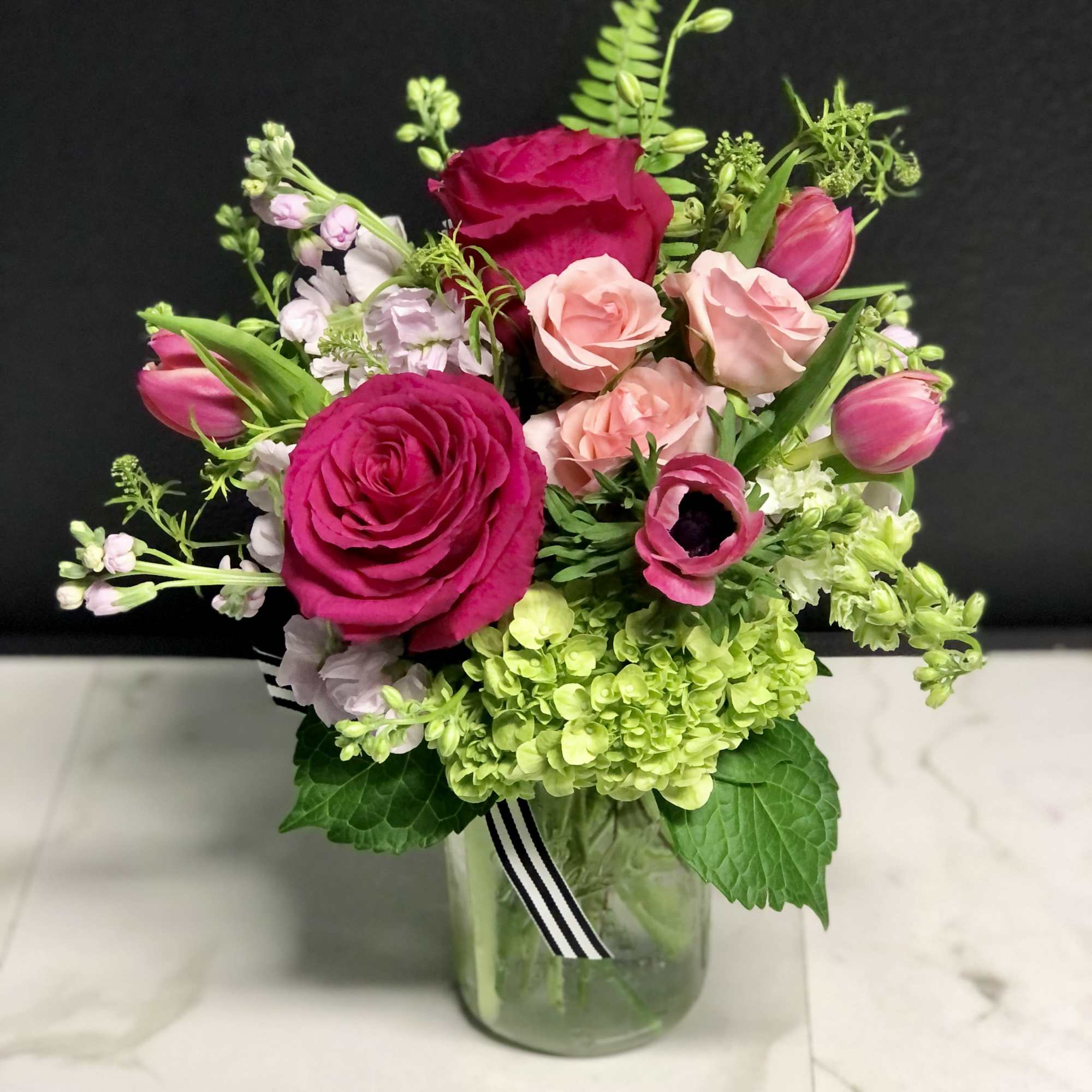 Bouquet of pink roses, tulips, and green hydrangea in a glass vase