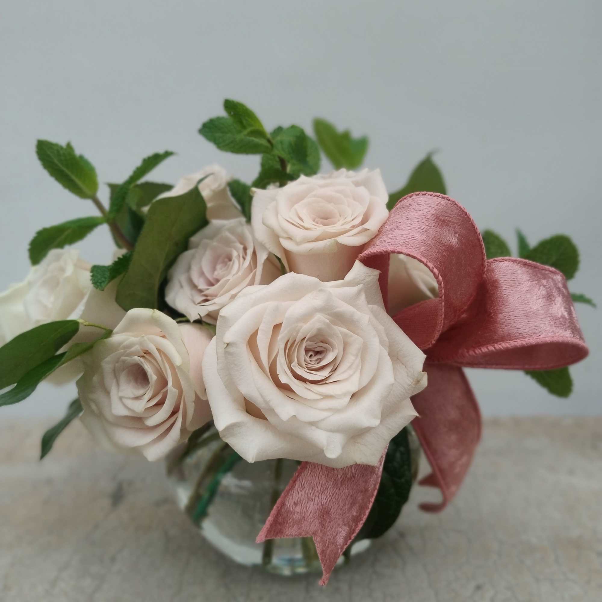 Twelve sand-colored roses with lemon leaf and mint accents, finished with a