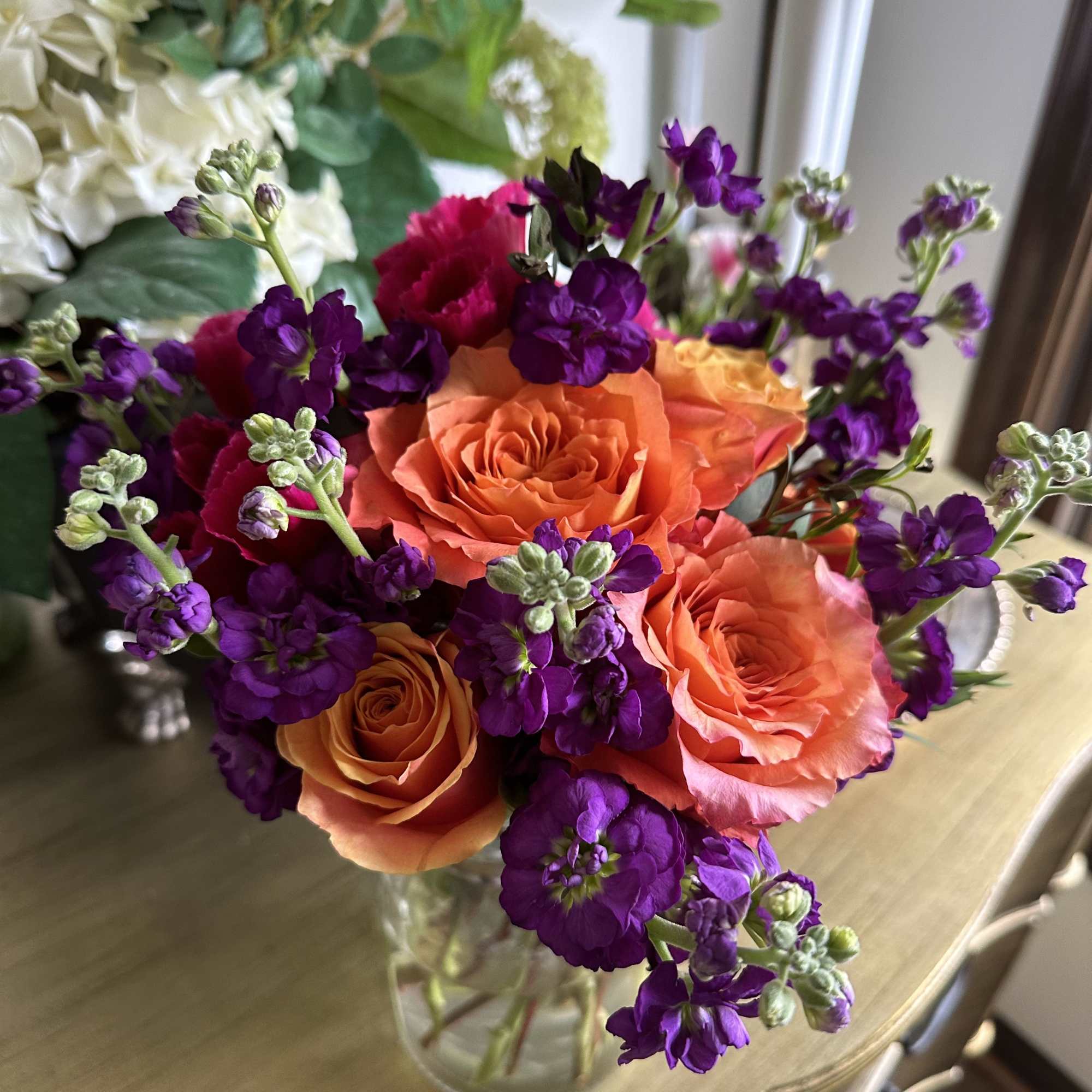 Orange roses and purple flowers in a clear glass vase
