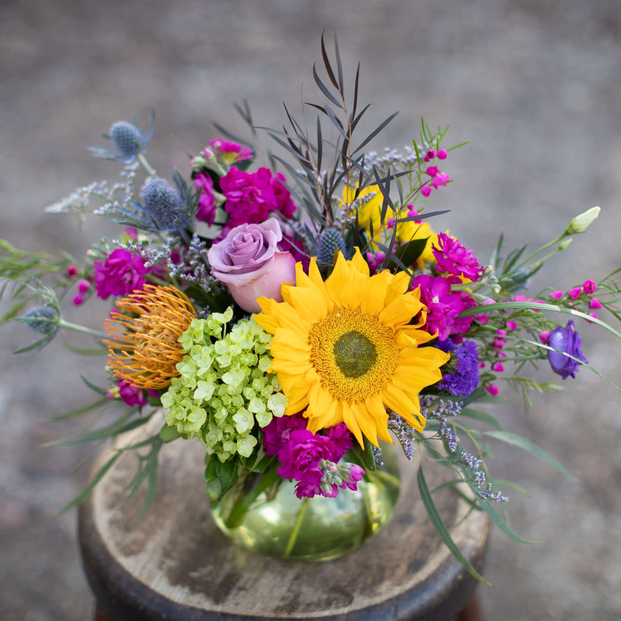 Colorful bouquet with a sunflower, roses, and purple blooms in a glass vase
