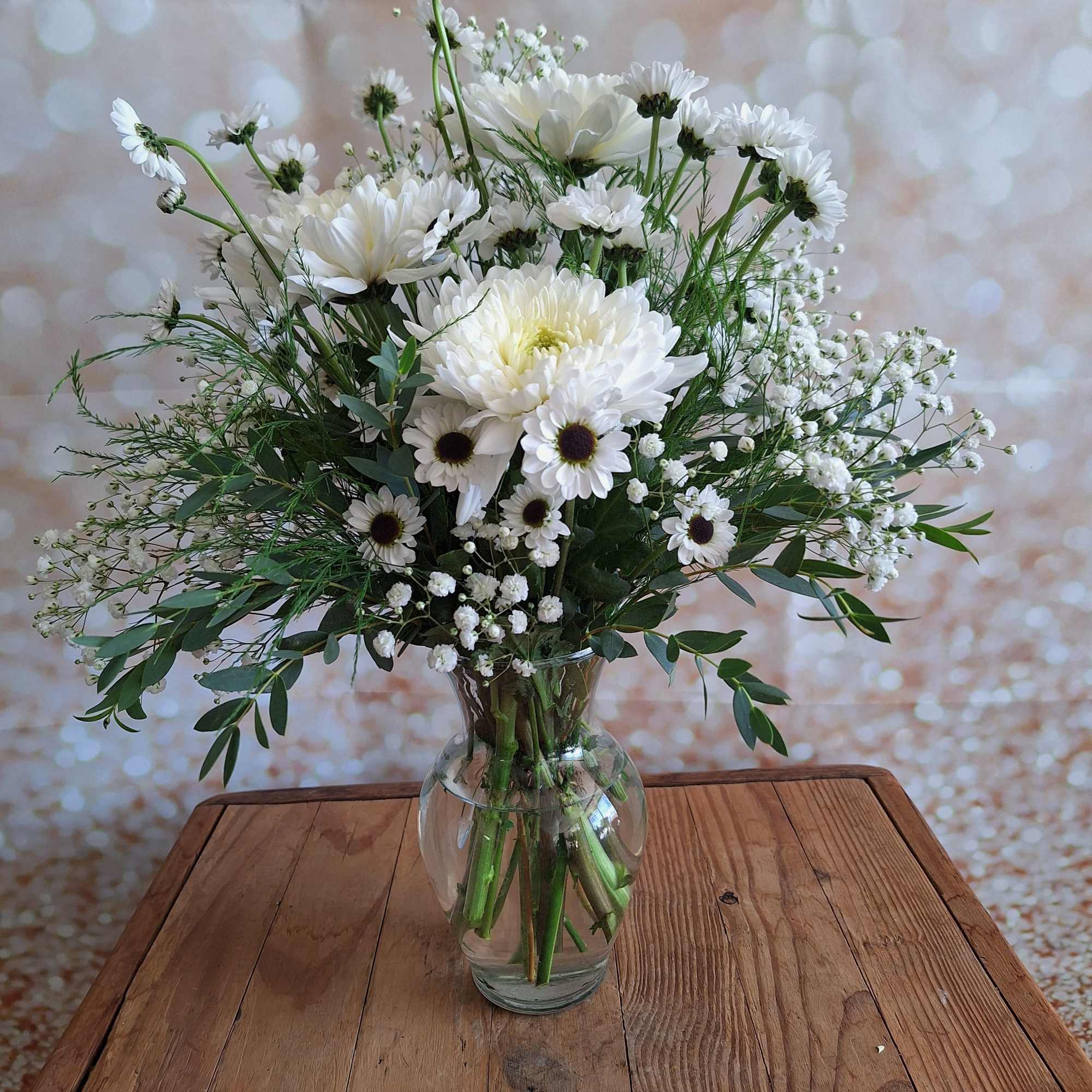White daisy bouquet in a clear glass vase on a wooden table