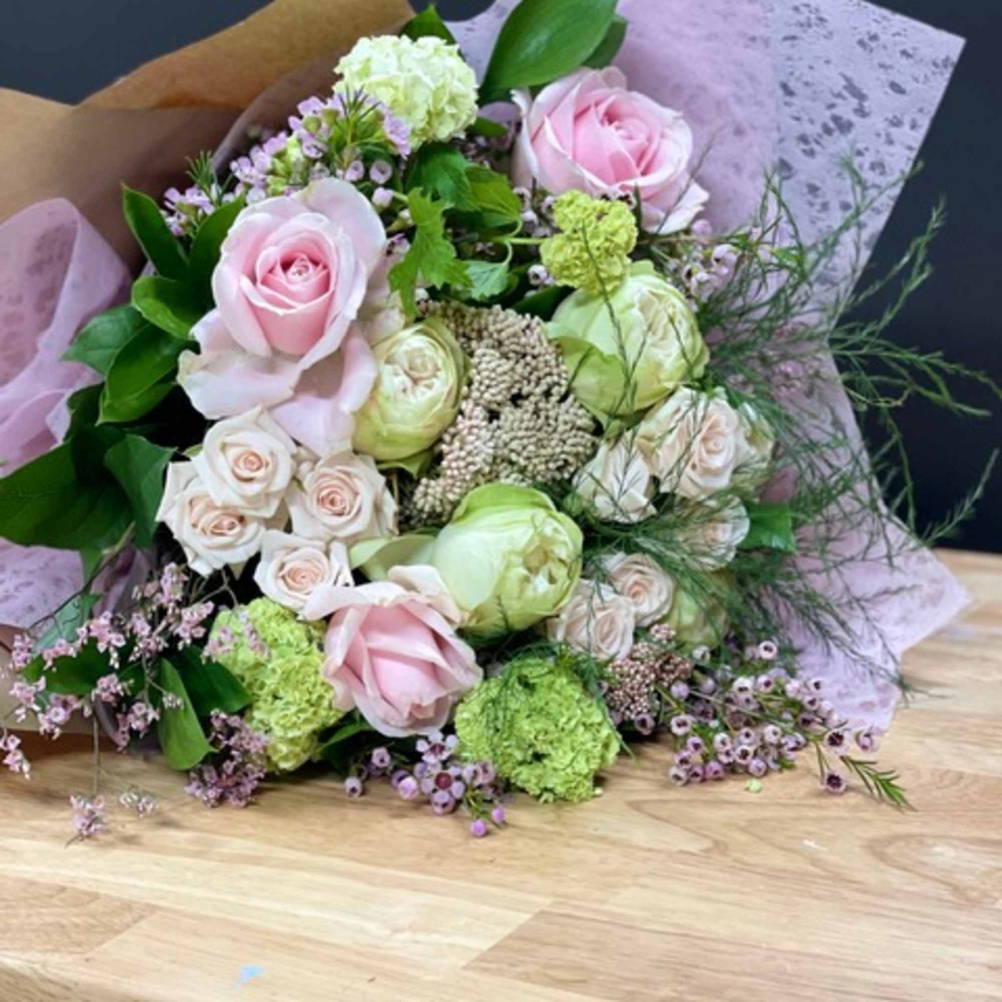Bouquet of pale pink and cream roses with green blooms wrapped in lavender paper