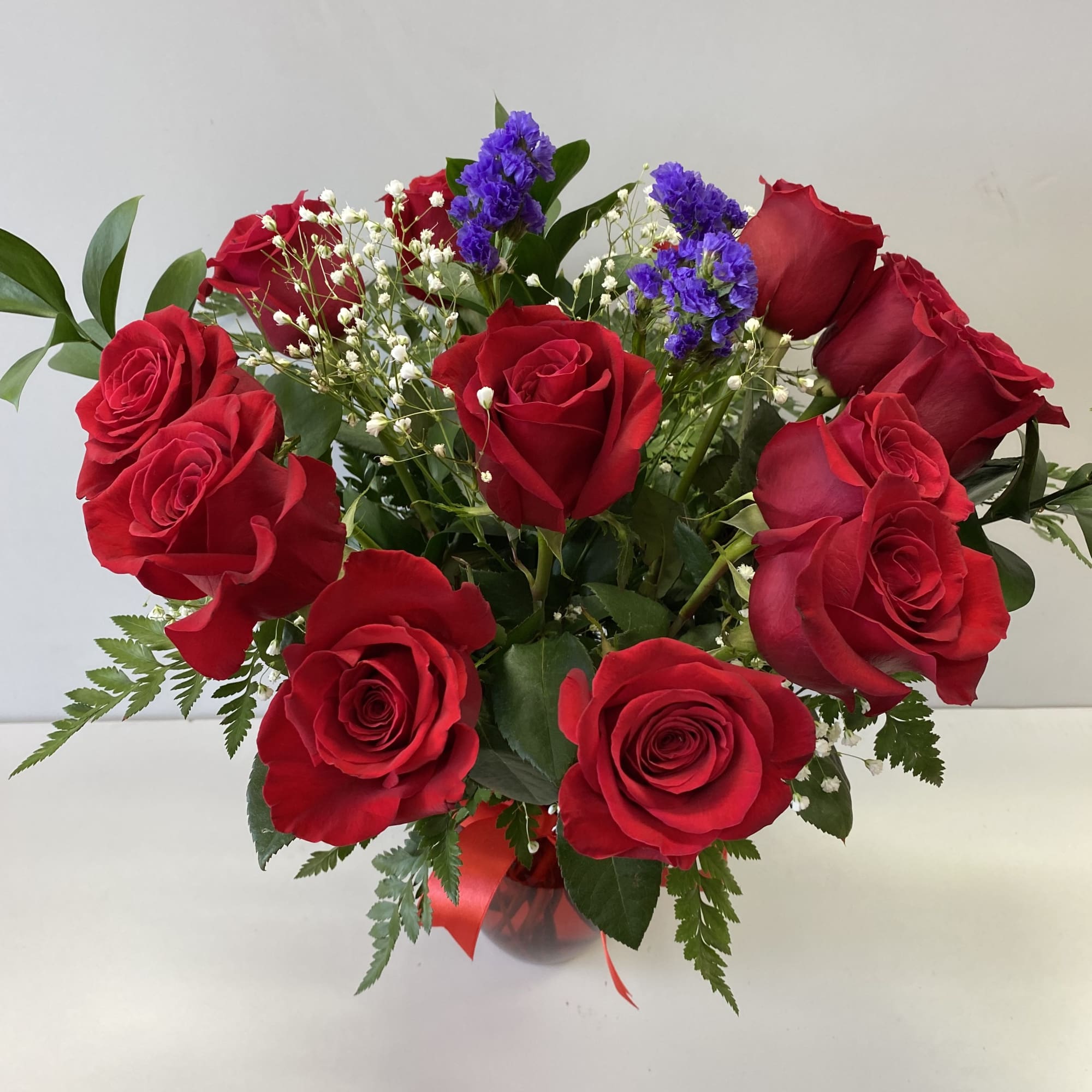 Arrangement of red roses with purple accent flowers and baby's breath in a red glass vase