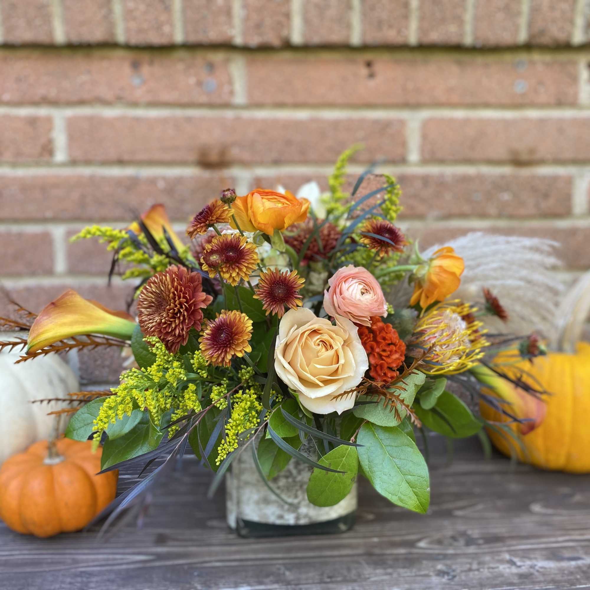 Autumn bouquet with roses and mums in a low vase, surrounded by pumpkins