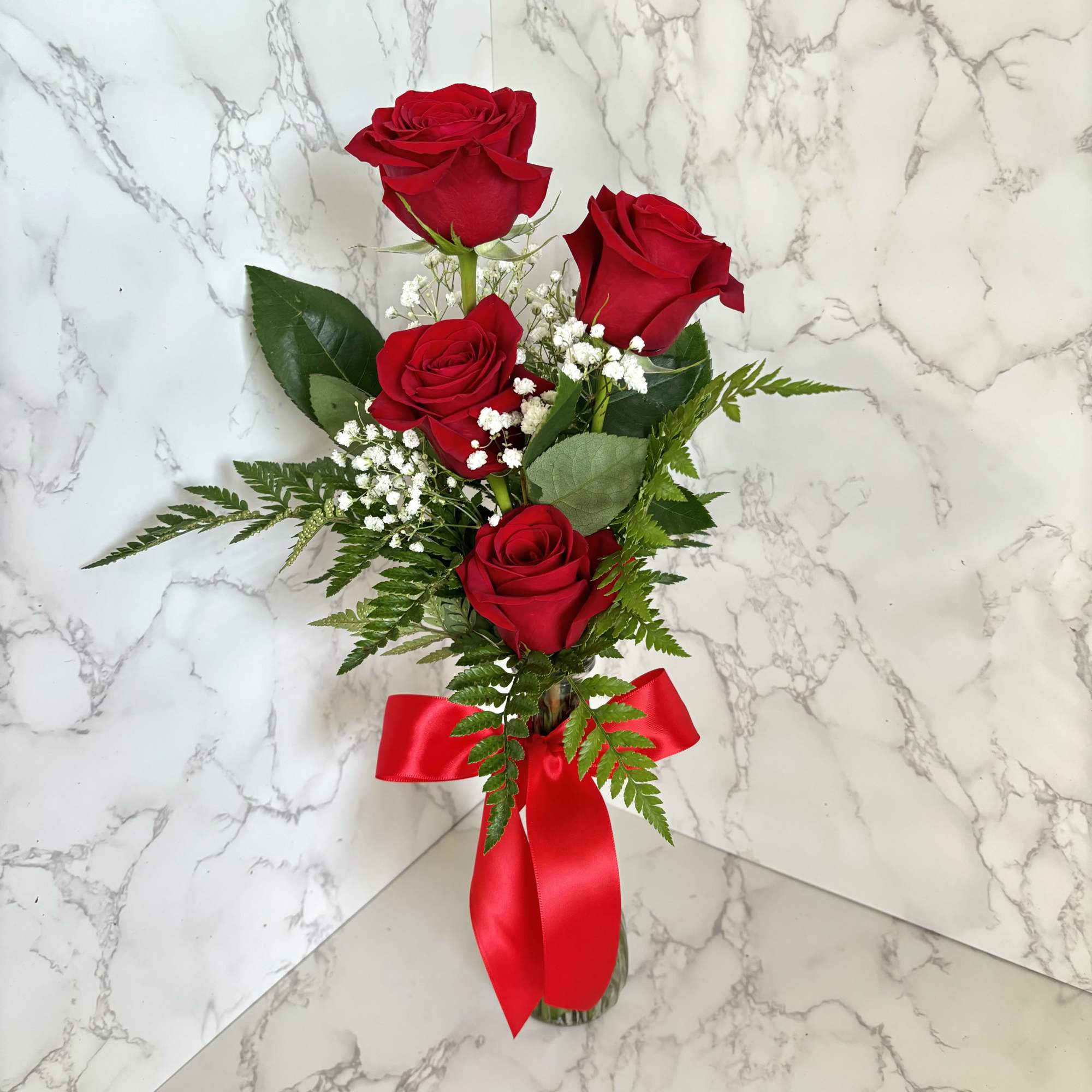 Bouquet of red roses with baby's breath in a glass vase and red ribbon