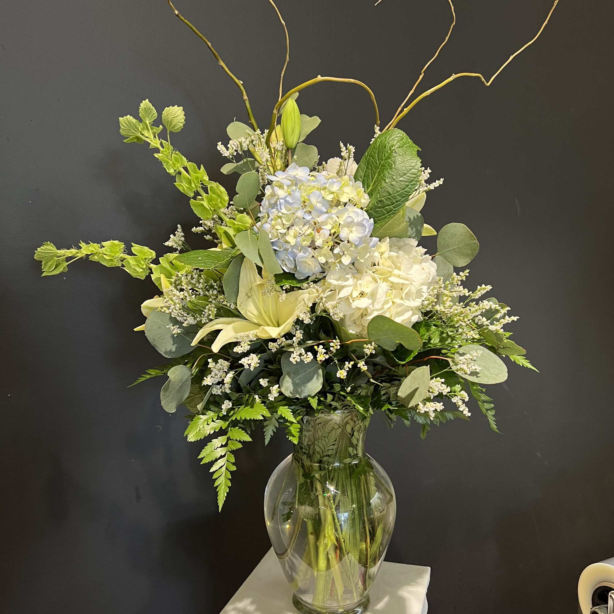 Tall white and pale blue floral arrangement in a glass vase