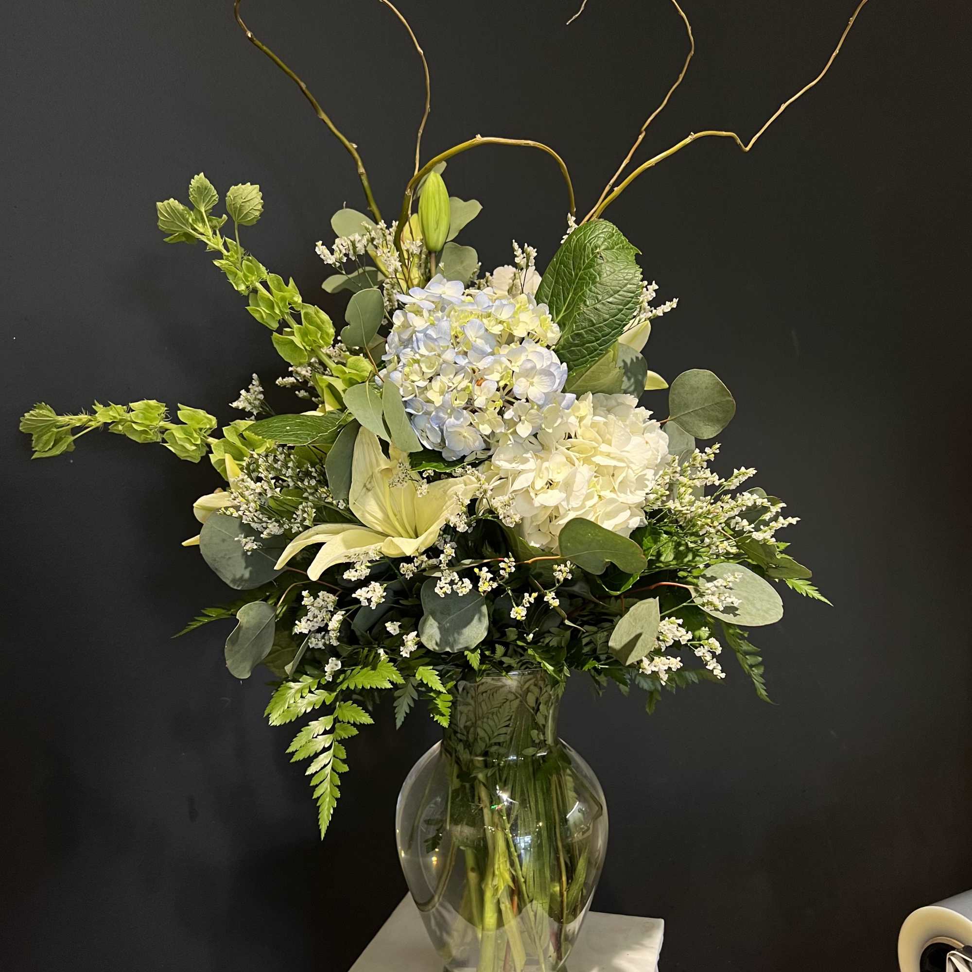 Tall floral arrangement in a glass vase with white and pale blue blooms
