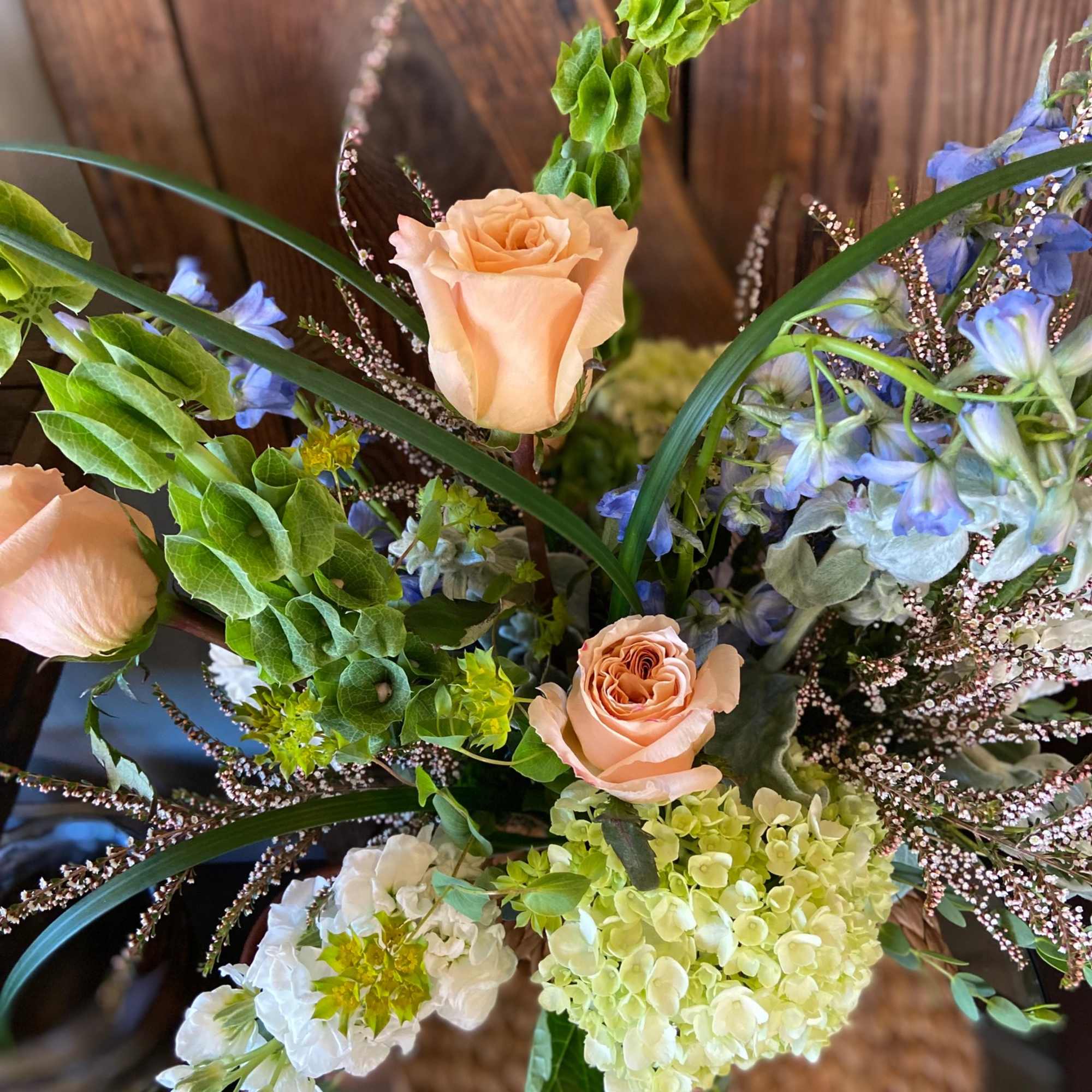 Peach roses with green hydrangeas, white blooms, and blue delphinium in a loose garden-style arrangement