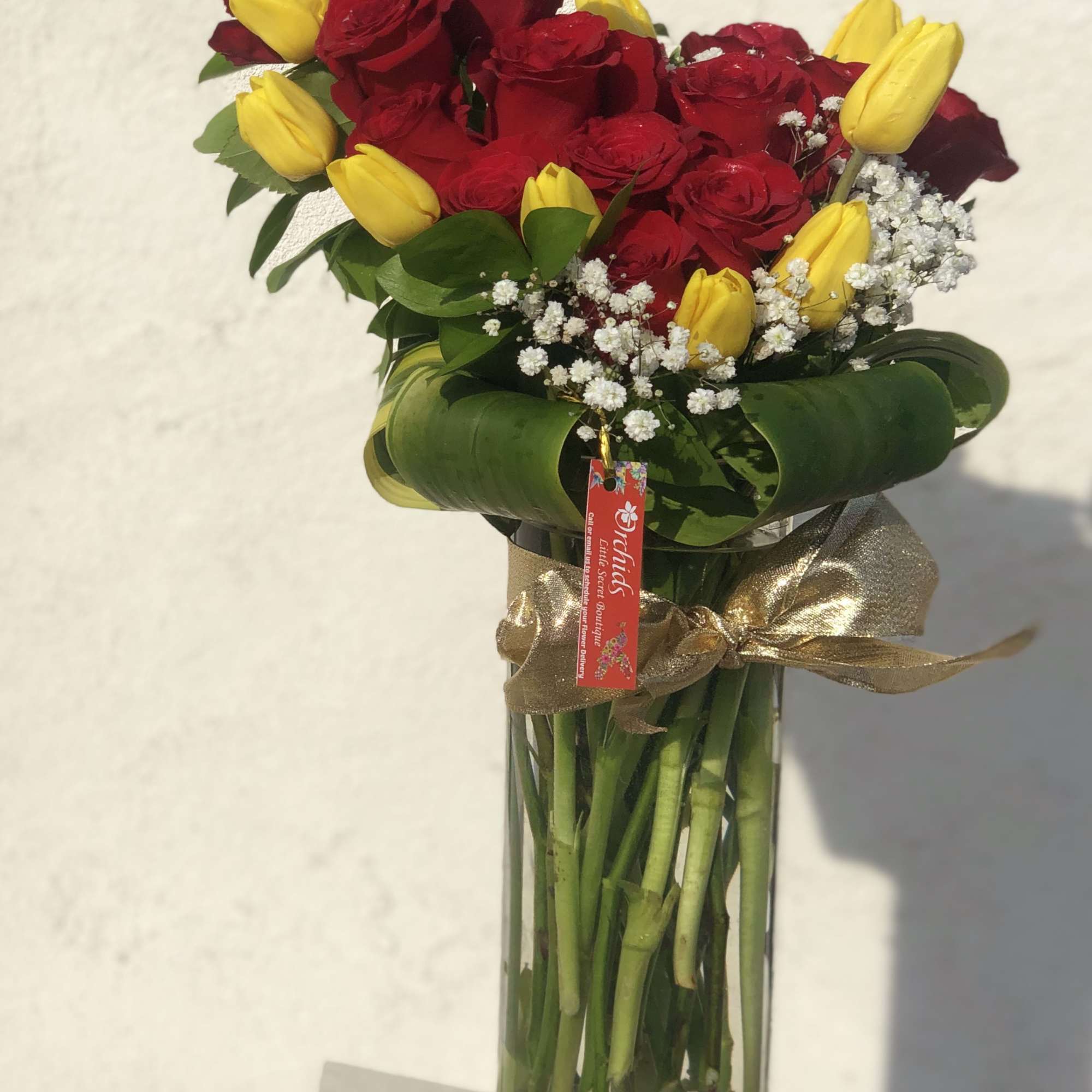 Bouquet of red roses and yellow tulips in a tall glass vase