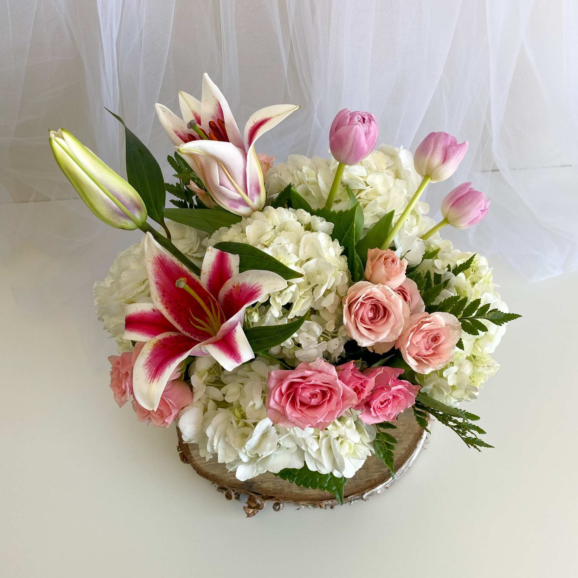 Pink lilies and roses arranged with white hydrangeas in a wood container