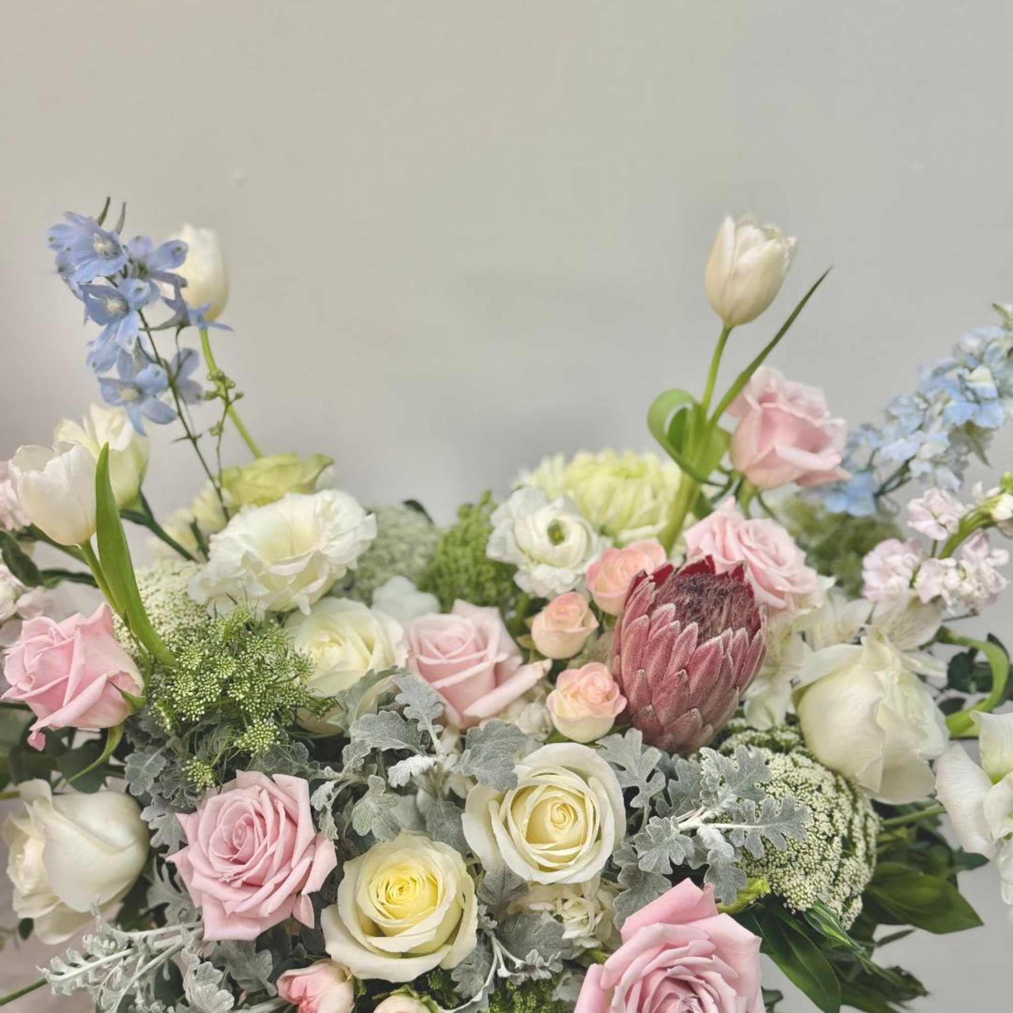 Pastel bouquet of roses, tulips, and blue flowers in a low vase