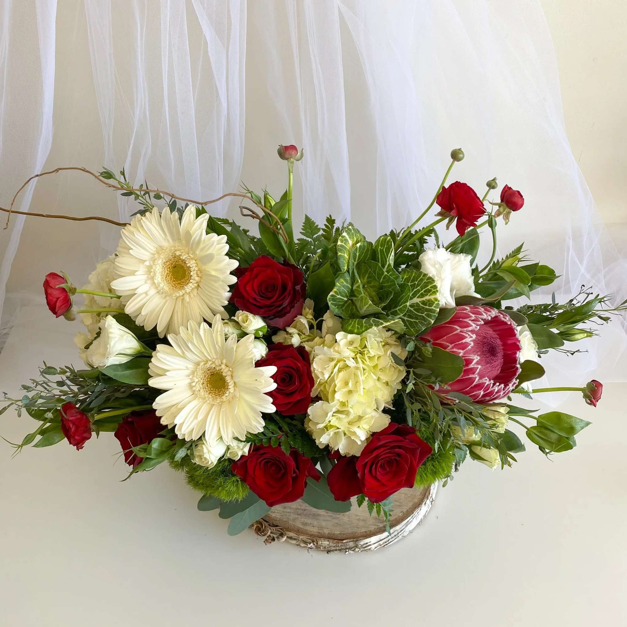 Mixed bouquet with red roses, white gerberas, and a pink protea in a rustic container