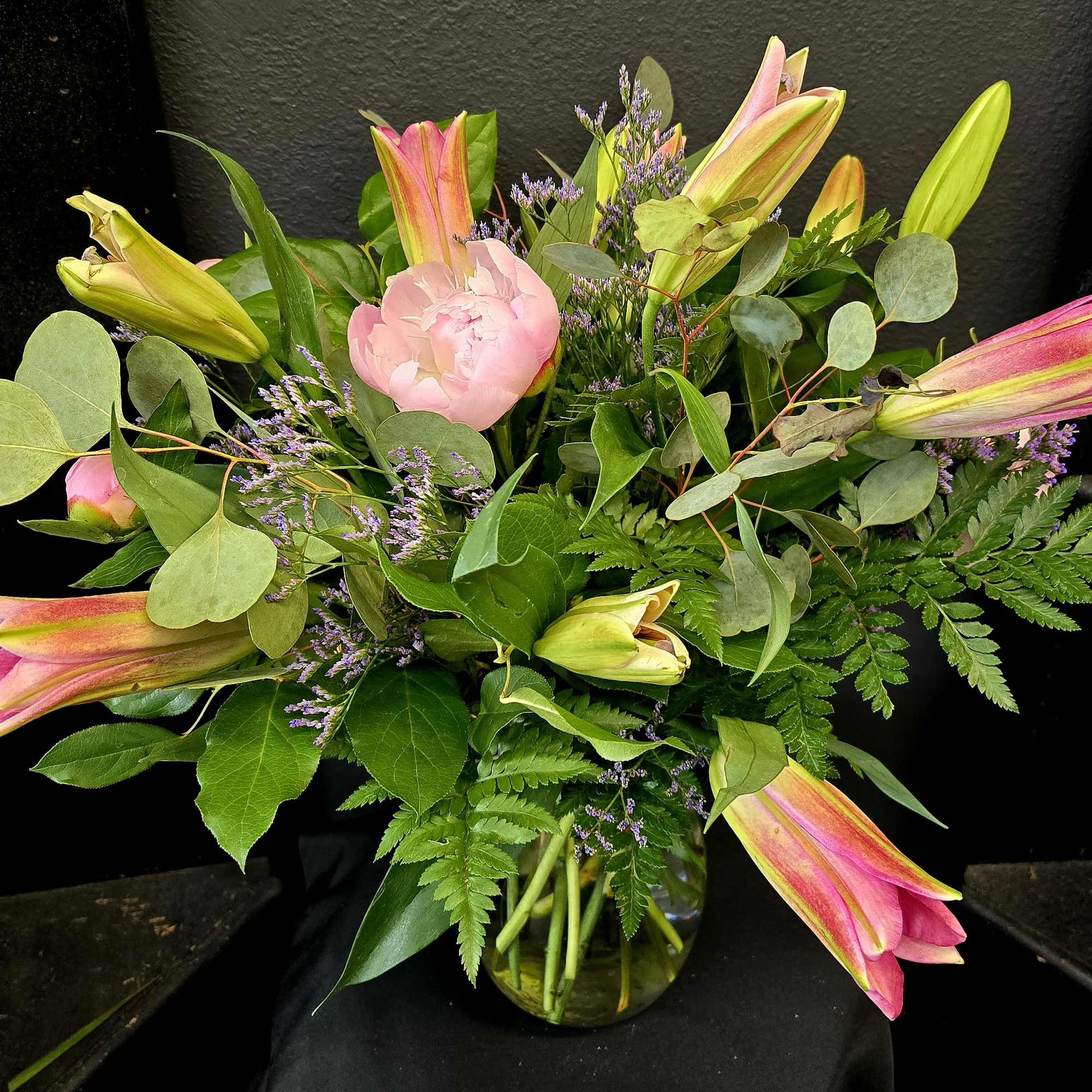 Pink lilies and a blush peony in a glass vase with mixed greenery