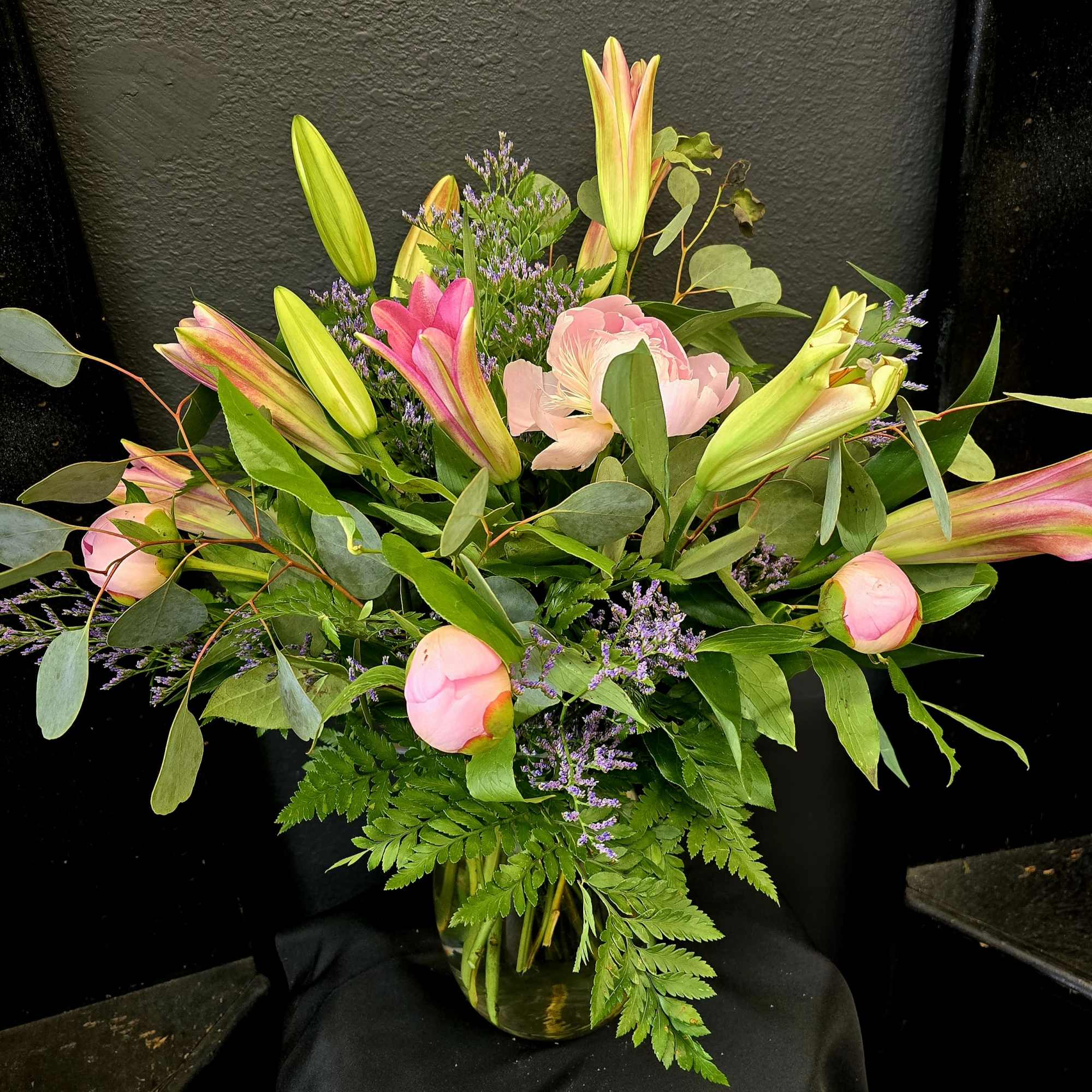 Pink lilies and peonies arranged in a glass vase with greenery.