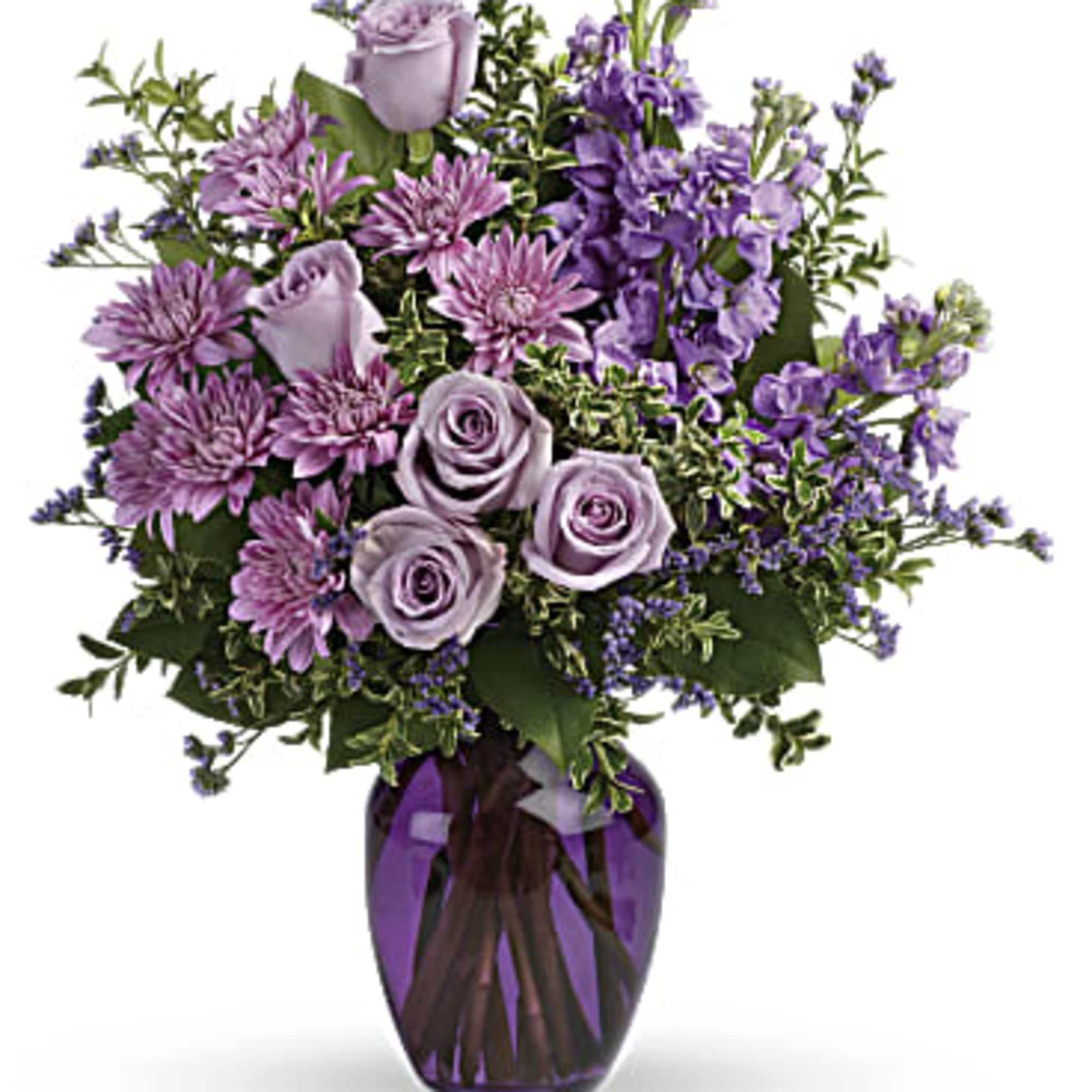 Lavender roses and purple flowers arranged in a glass vase