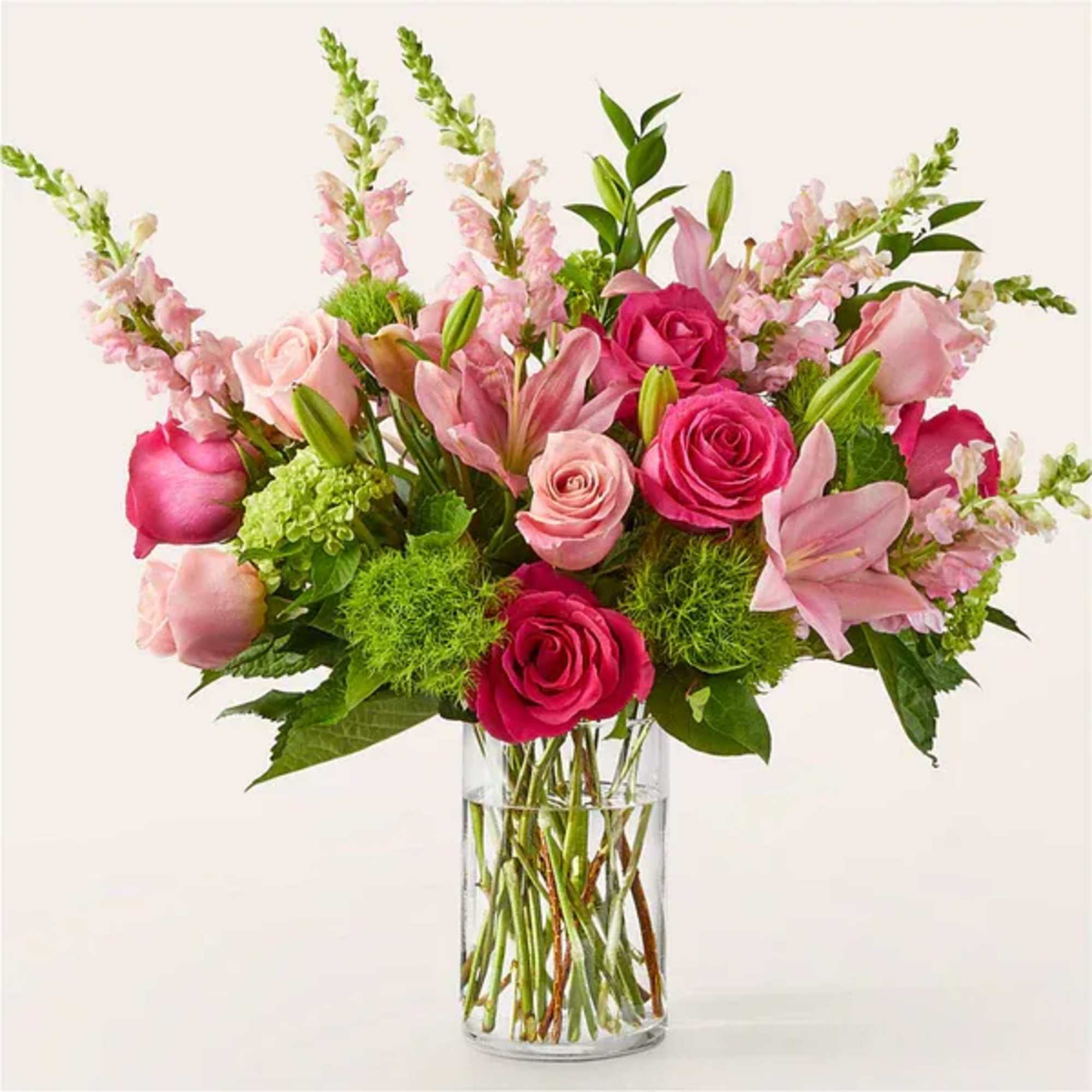 Pink roses, lilies, and snapdragons arranged with green accents in a clear glass cylinder vase